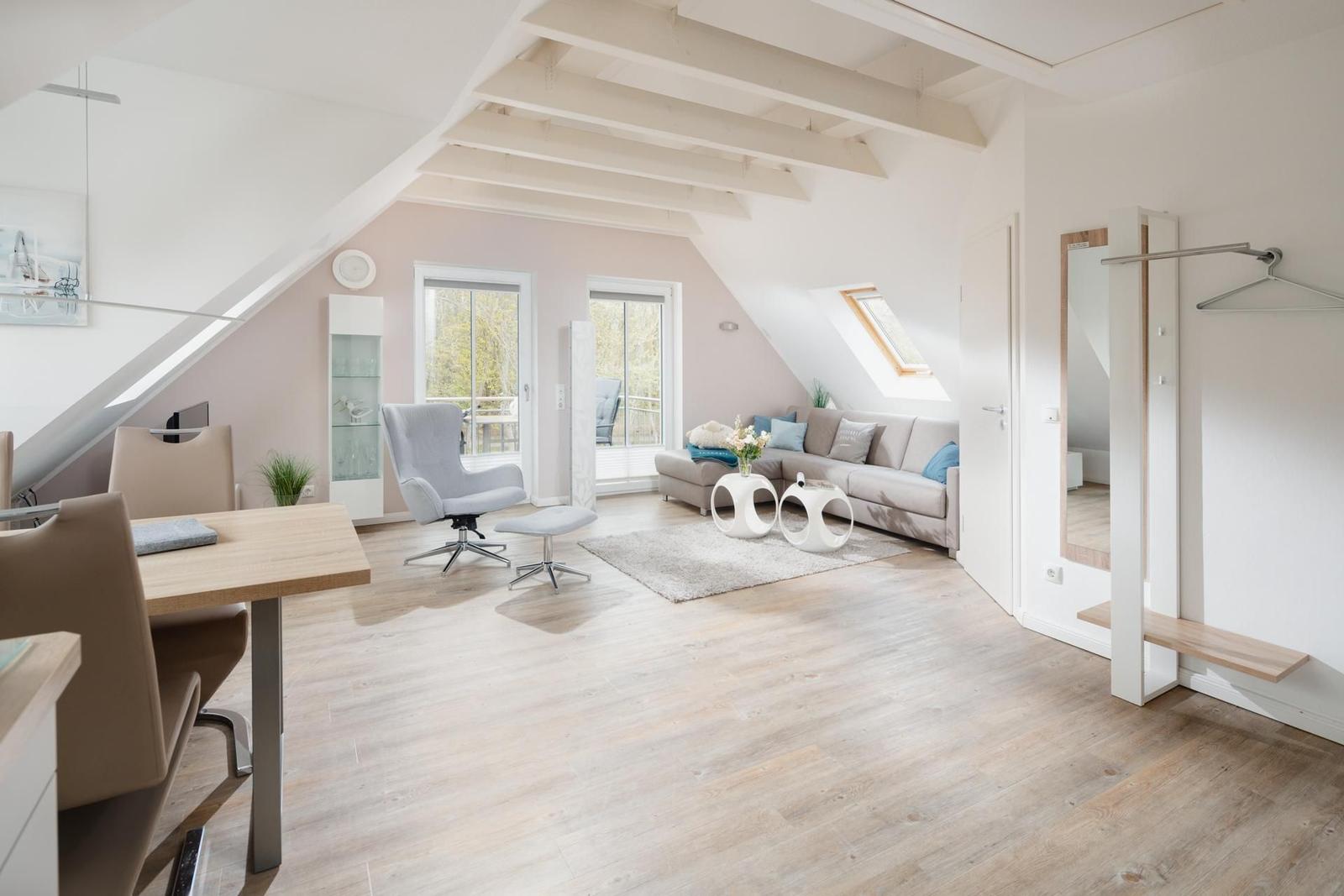 Wohn- und Essbereich mit Sofa, Tisch und Stühlen. Holzboden und weiße Balken.