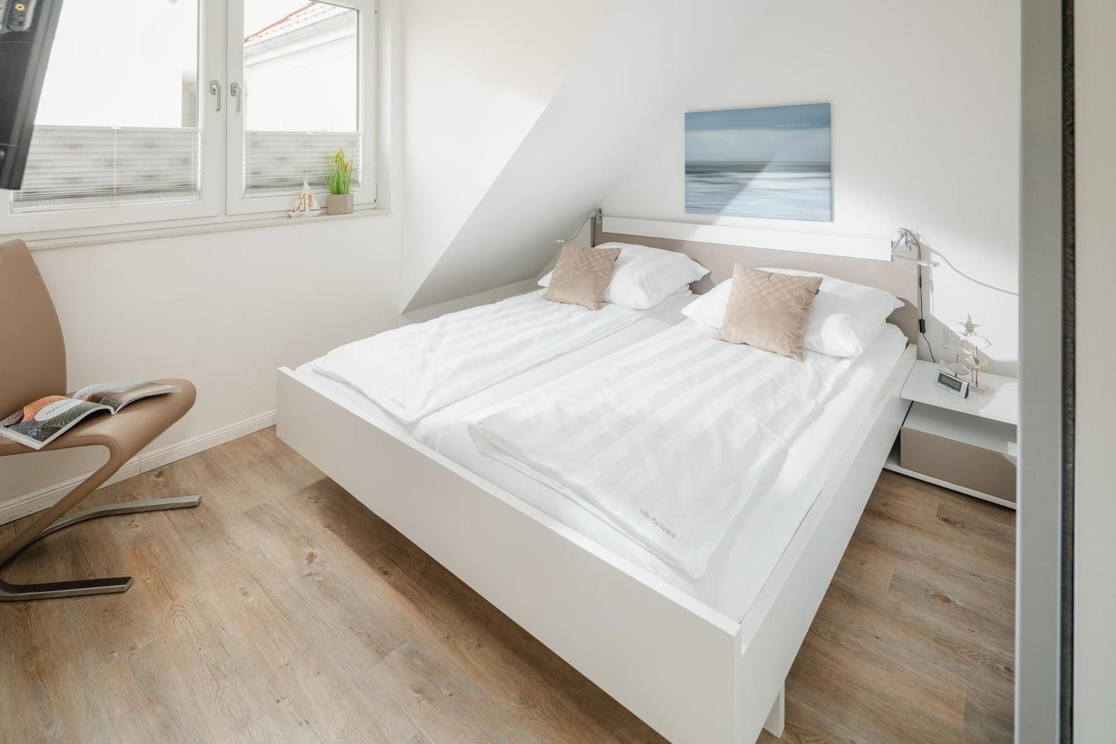 Schlafzimmer mit Doppelbett, Fenster und Nachttisch.
