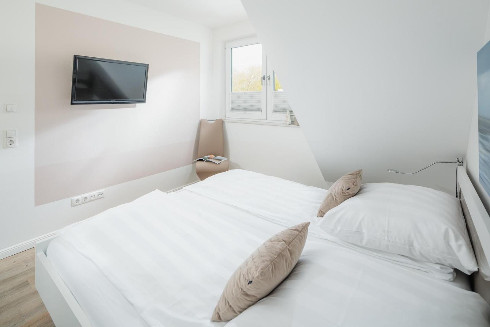 Schlafzimmer mit Doppelbett, Wand-TV und Fenster.