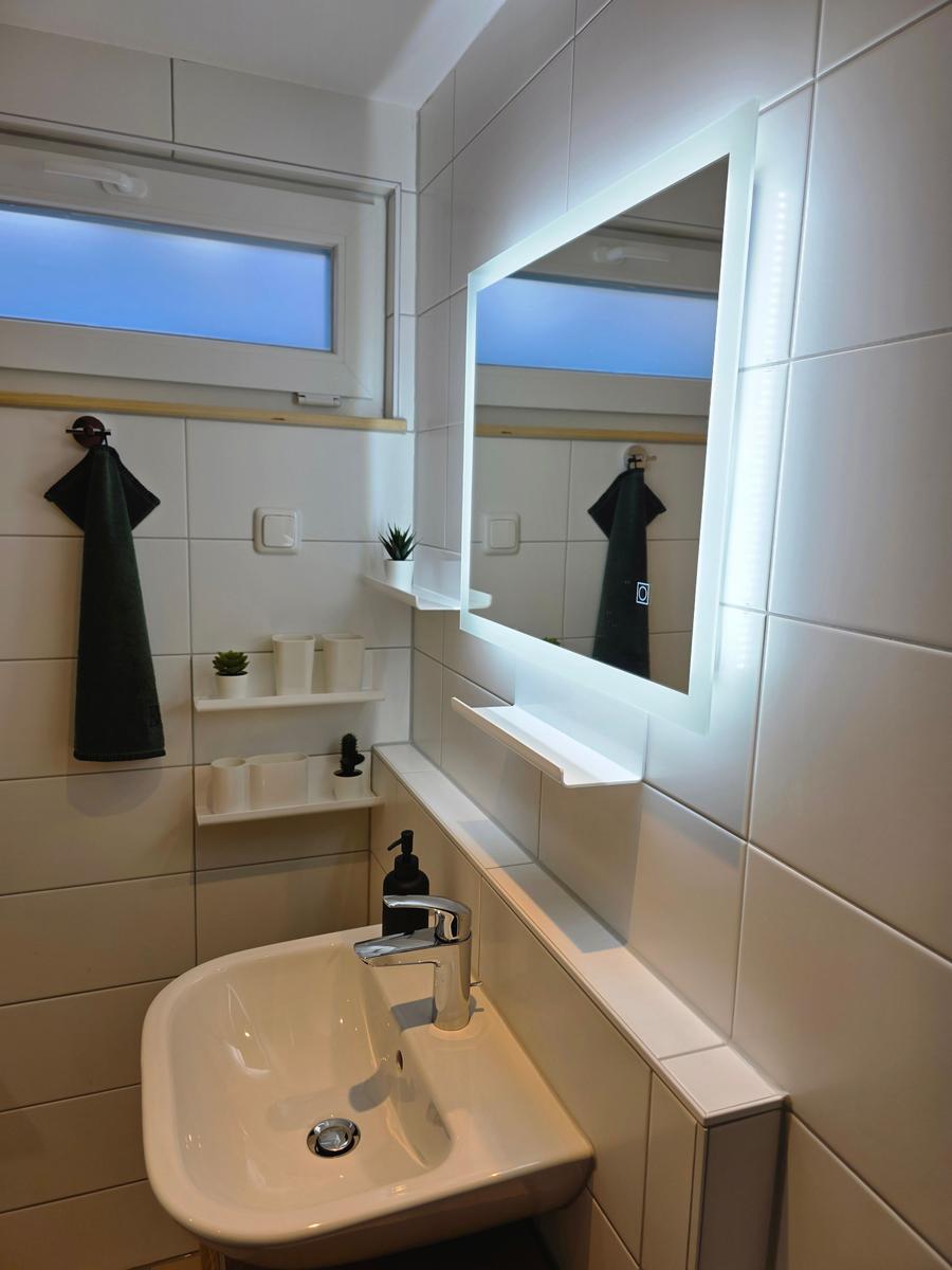 Badezimmer mit Waschbecken, beleuchtetem Spiegel und Fenster.