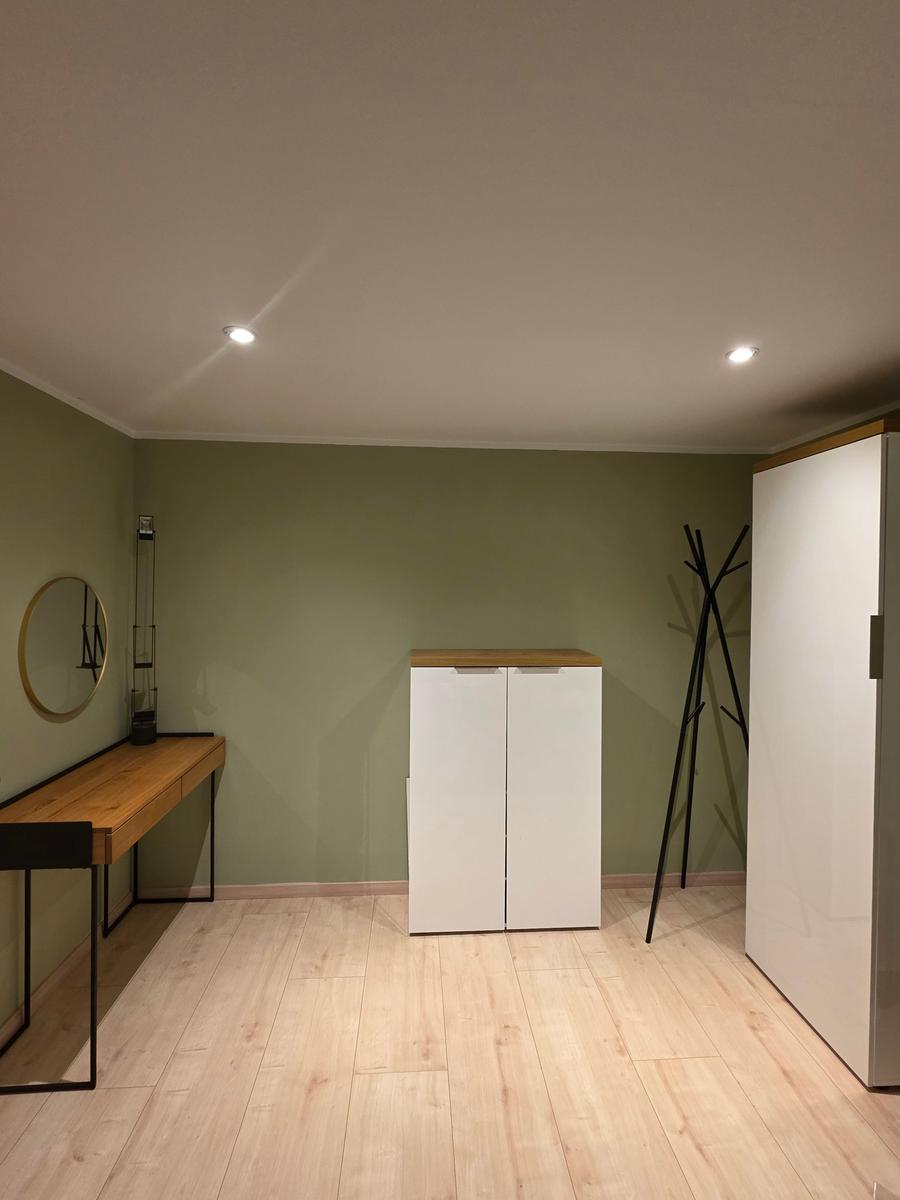 Ein Zimmer mit Holzboden, grünen Wänden, Schreibtisch, Kleiderständer und Schrank.