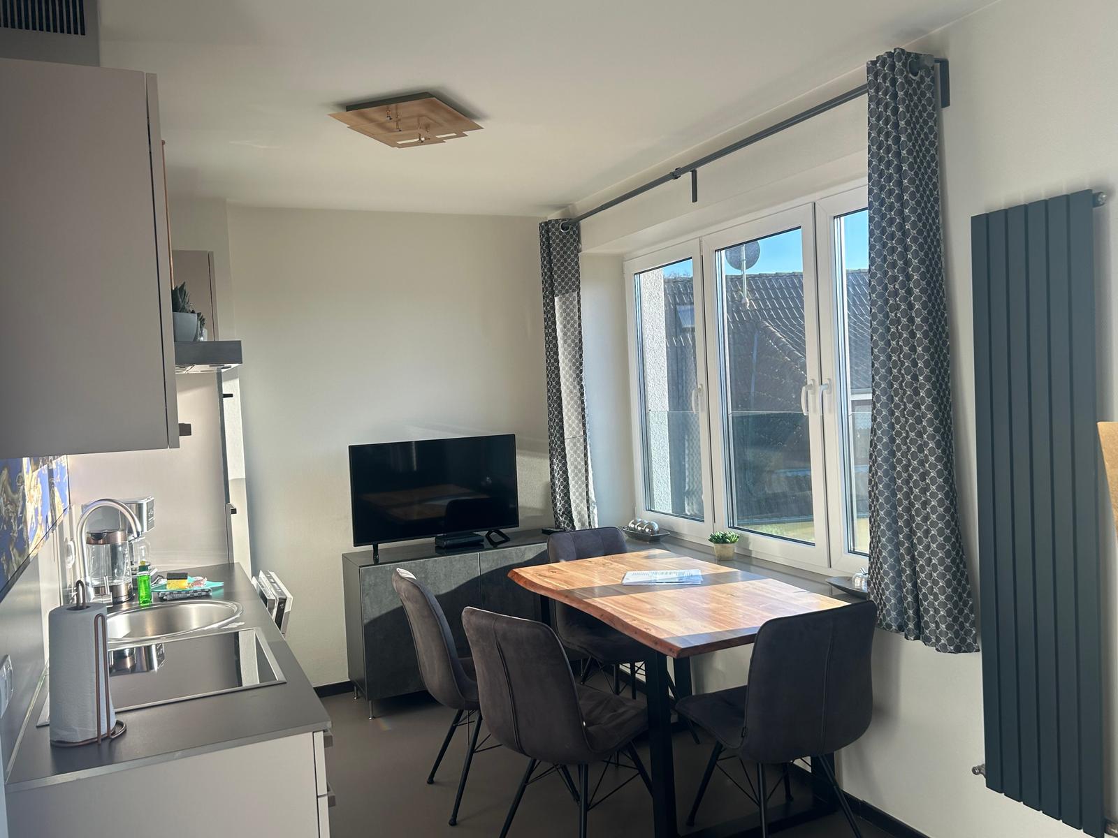 Küche, Essbereich mit Tisch und Stühlen, Fernseher und Fenster.