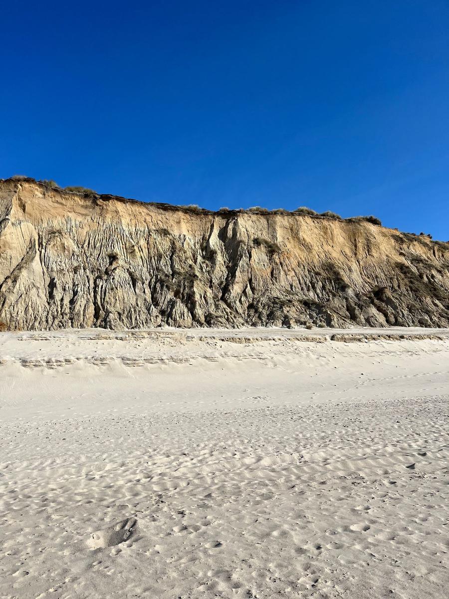 Weiterer Blick auf die weiße Sandküste mit steilen Felsformationen im Hintergrund.