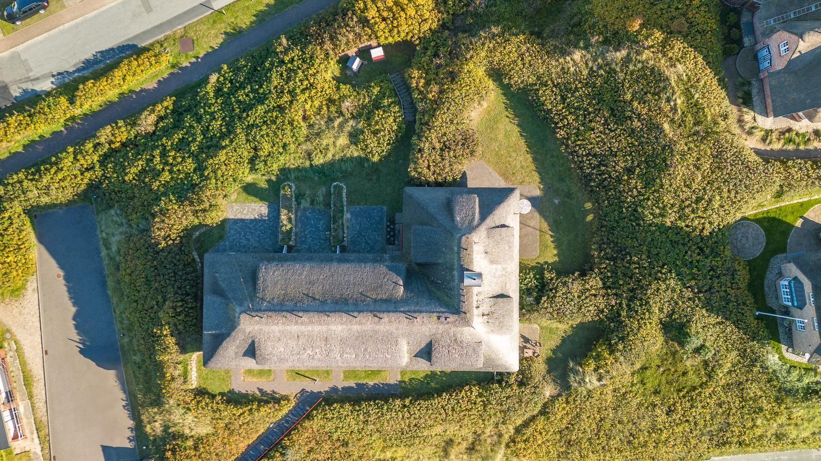 Haus mit Dach aus Stroh, umgeben von Grünflächen und einem Weg.