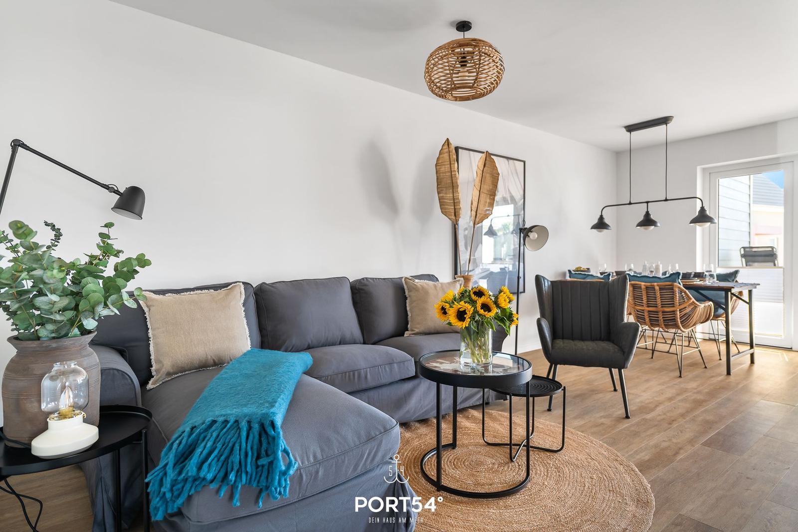 Ein Wohn- und Essbereich mit grauem Sofa, Holzboden und moderner Beleuchtung.