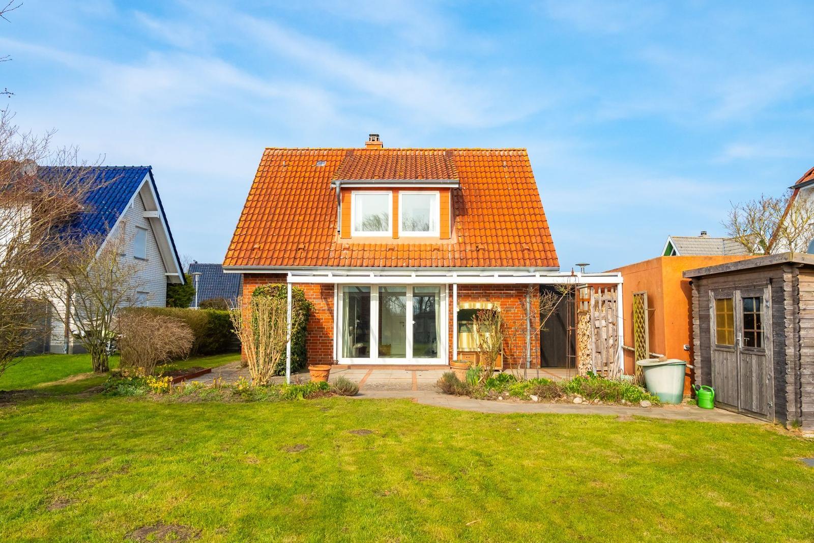 Haus mit orangefarbenem Dach und Garten. Nebenhaus und Holzschuppen sind sichtbar.