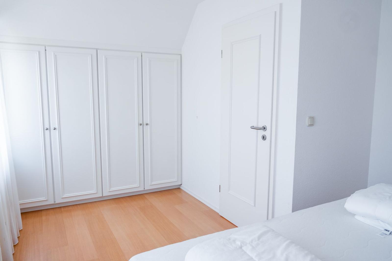Schlafzimmer mit weißem Schrank, Bett und Holzboden.