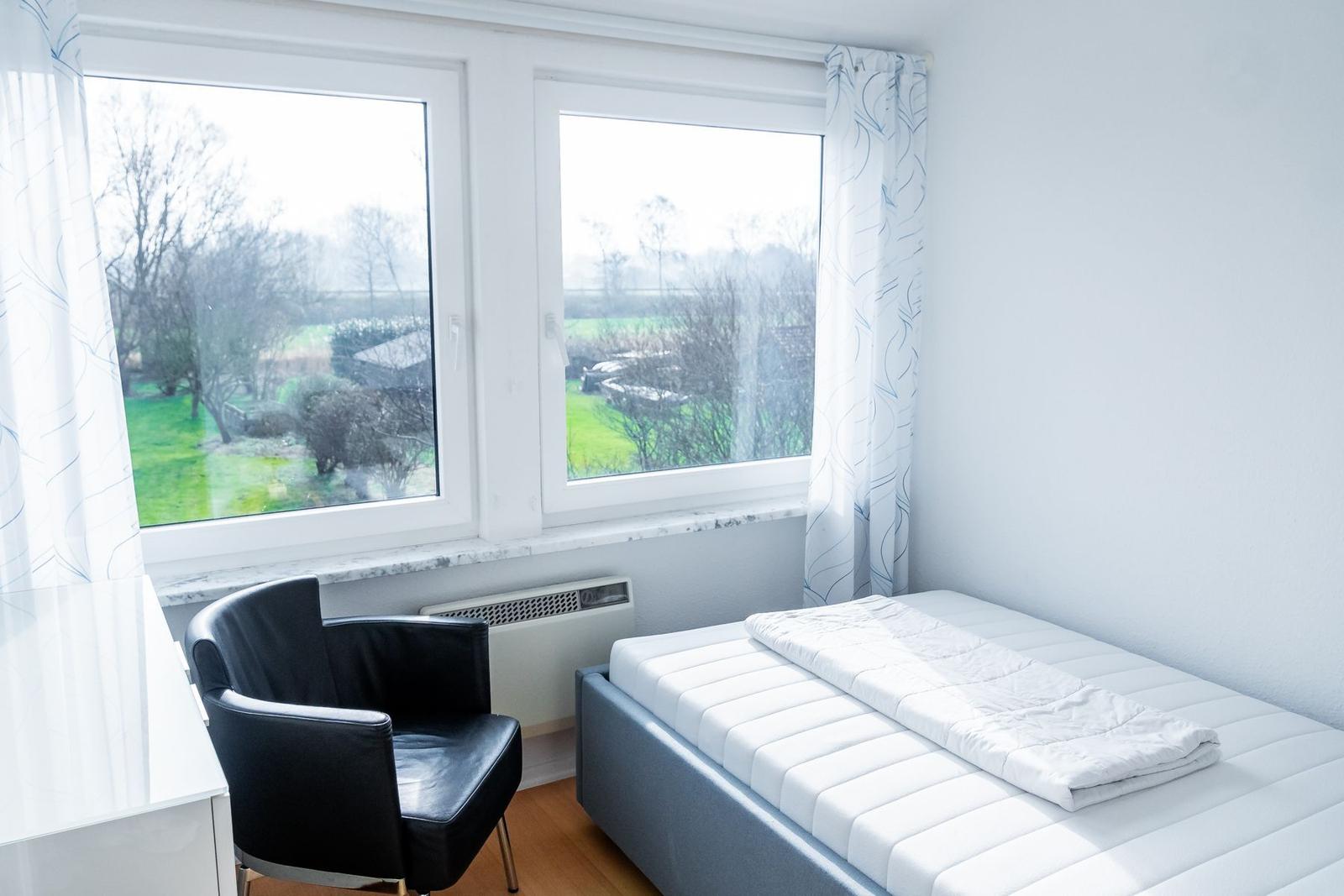 Schlafzimmer mit Bett, Stuhl und Fensterblick auf Garten