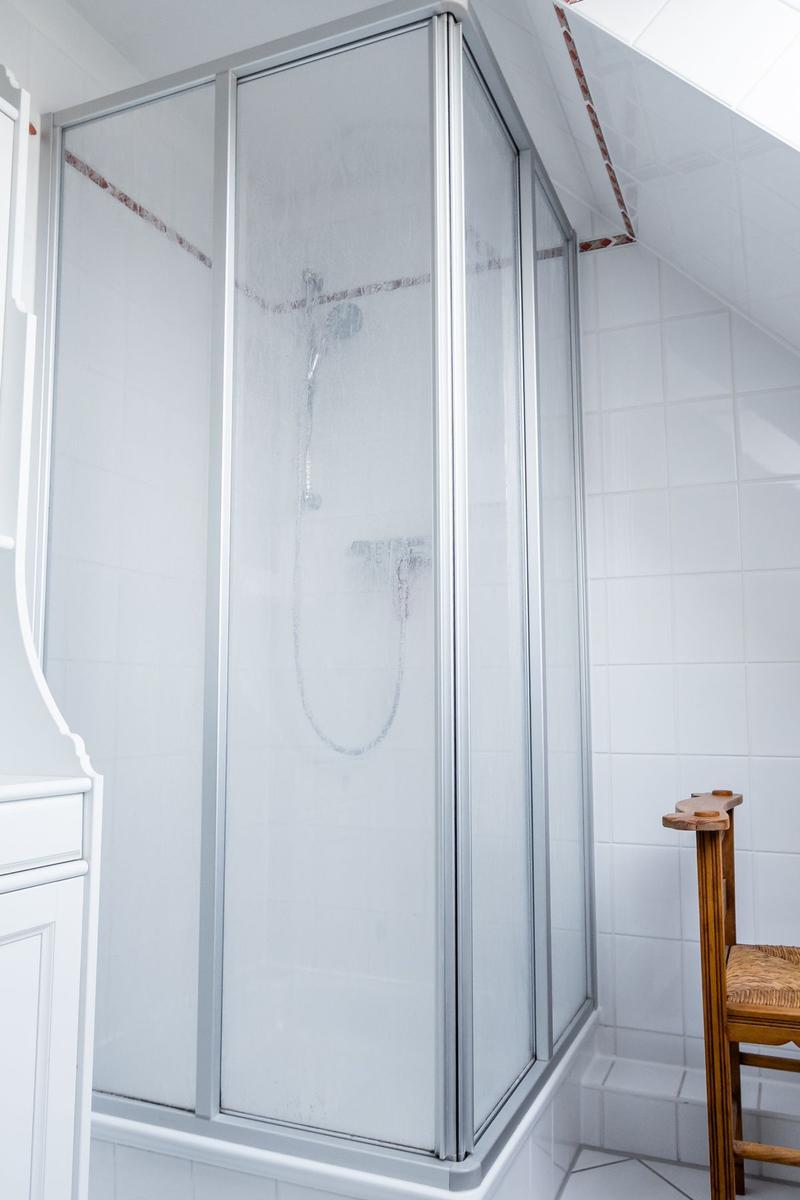 Duschkabine mit Glaswand und Duschbrause in weißer Fliesenwand