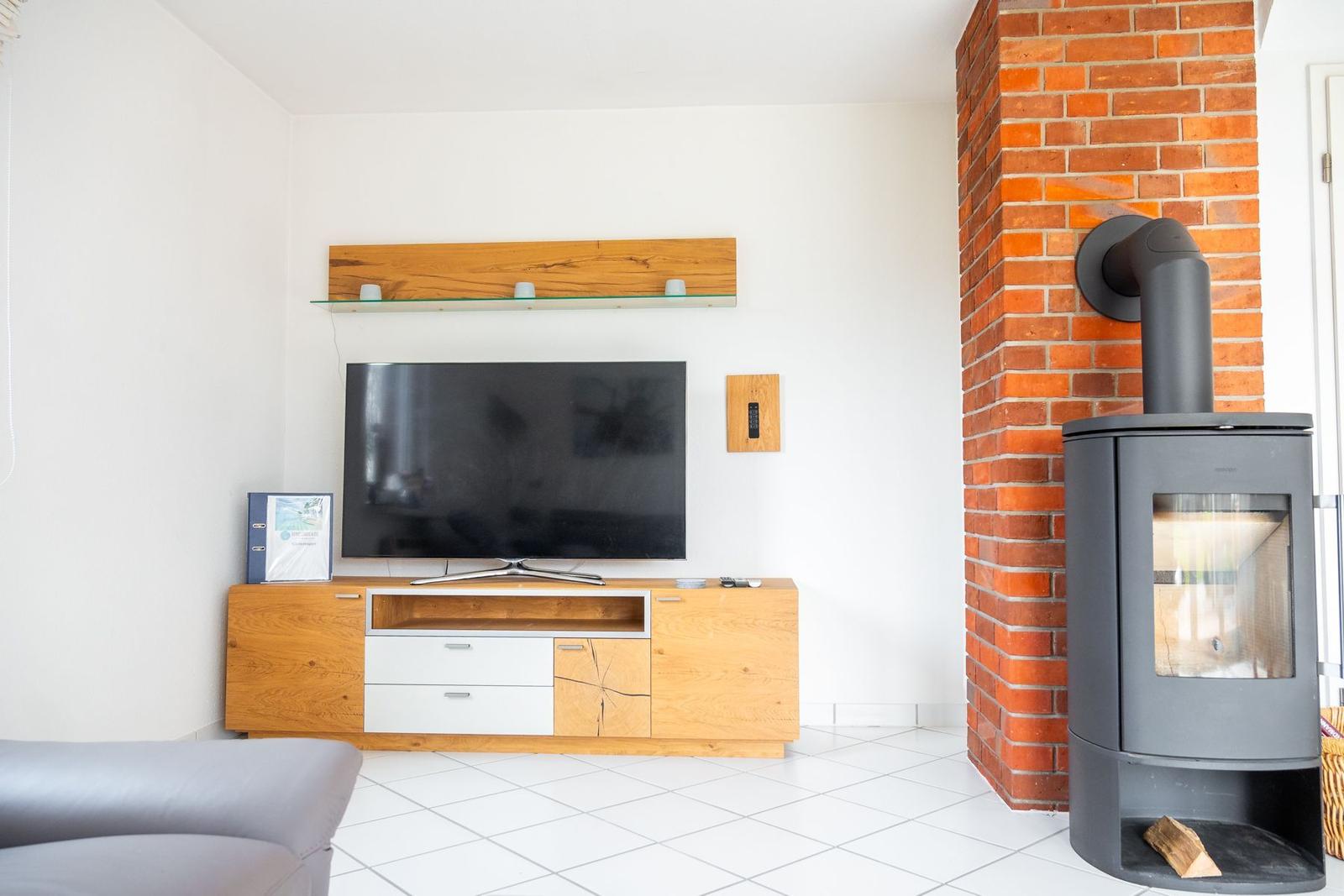 Wohnzimmer mit Fernseher, Holzmöbel und Kaminofen an Backsteinwand.