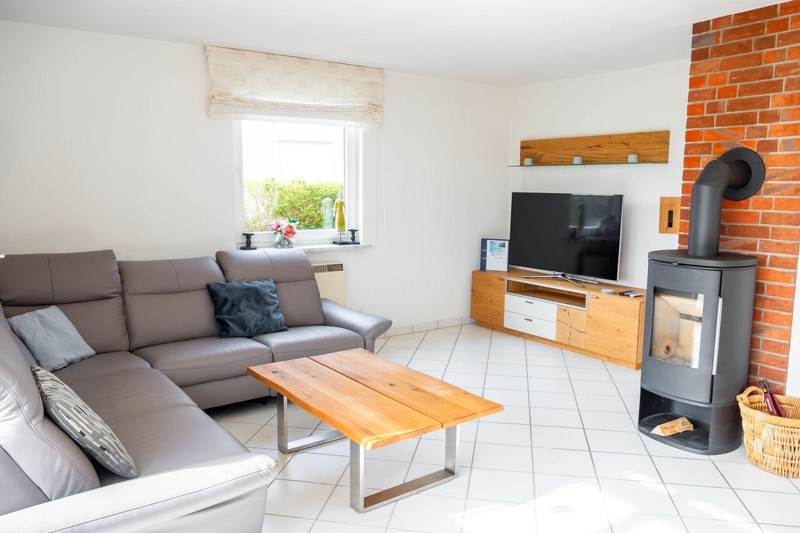 Wohnzimmer mit Sofa, TV und Kaminofen an Backsteinwand.