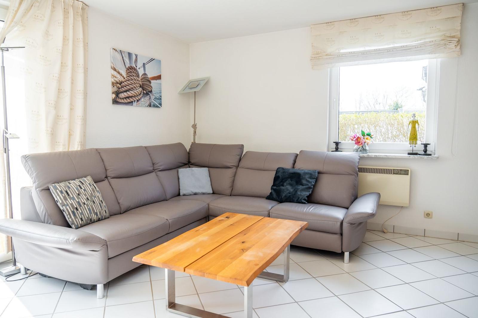 Ein Wohnzimmer mit braunem Sofa, Holztisch und Fenster mit Blick nach draußen.