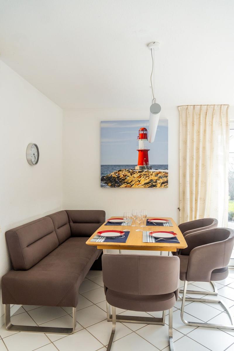 Esszimmer mit braunem Sofa, Tisch und Stühlen. Wandbild zeigt Leuchtturm.