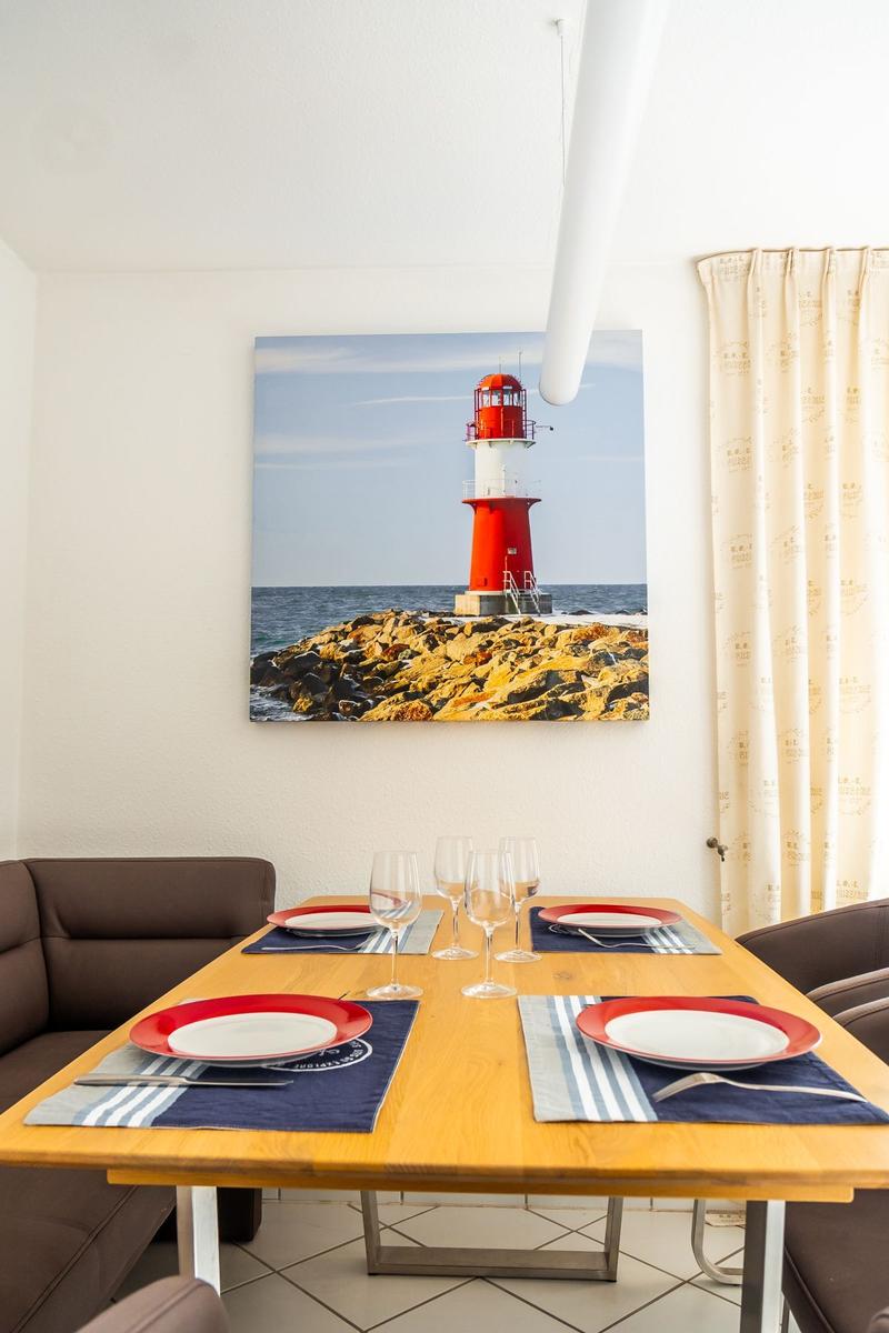 Esszimmer mit Tisch, Stühlen und Leuchtturm-Bild an der Wand.