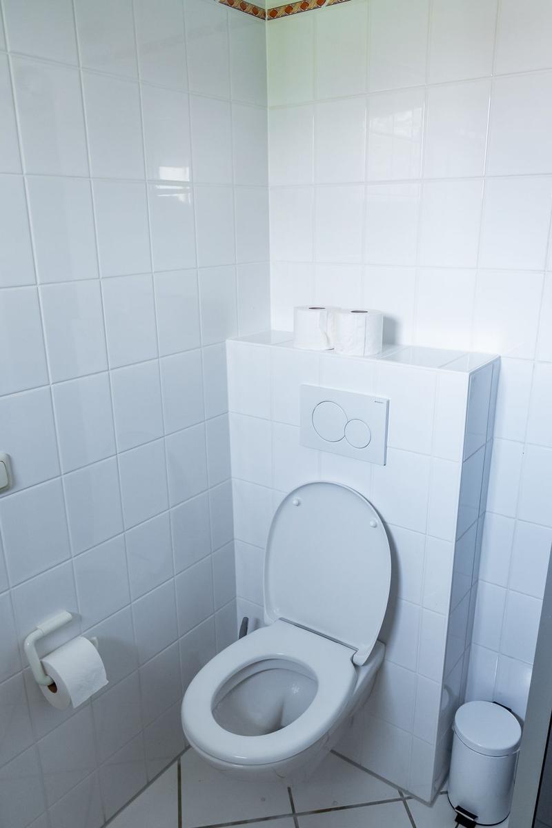 Toilette mit Toilettenpapier und Mülleimer in weißer Fliesenwand