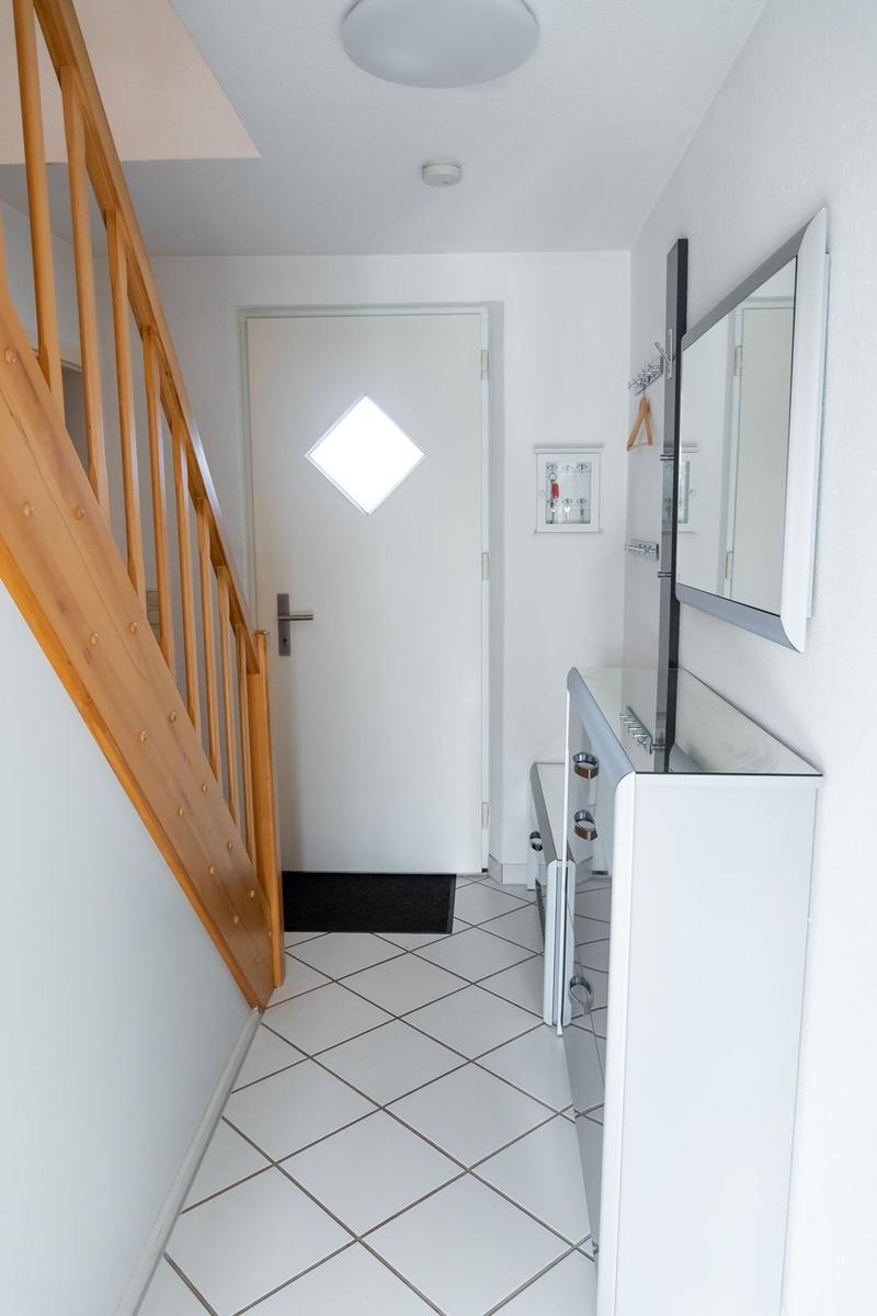 Eingangsbereich mit Holzgeländer, weiße Tür und Spiegelschrank.
