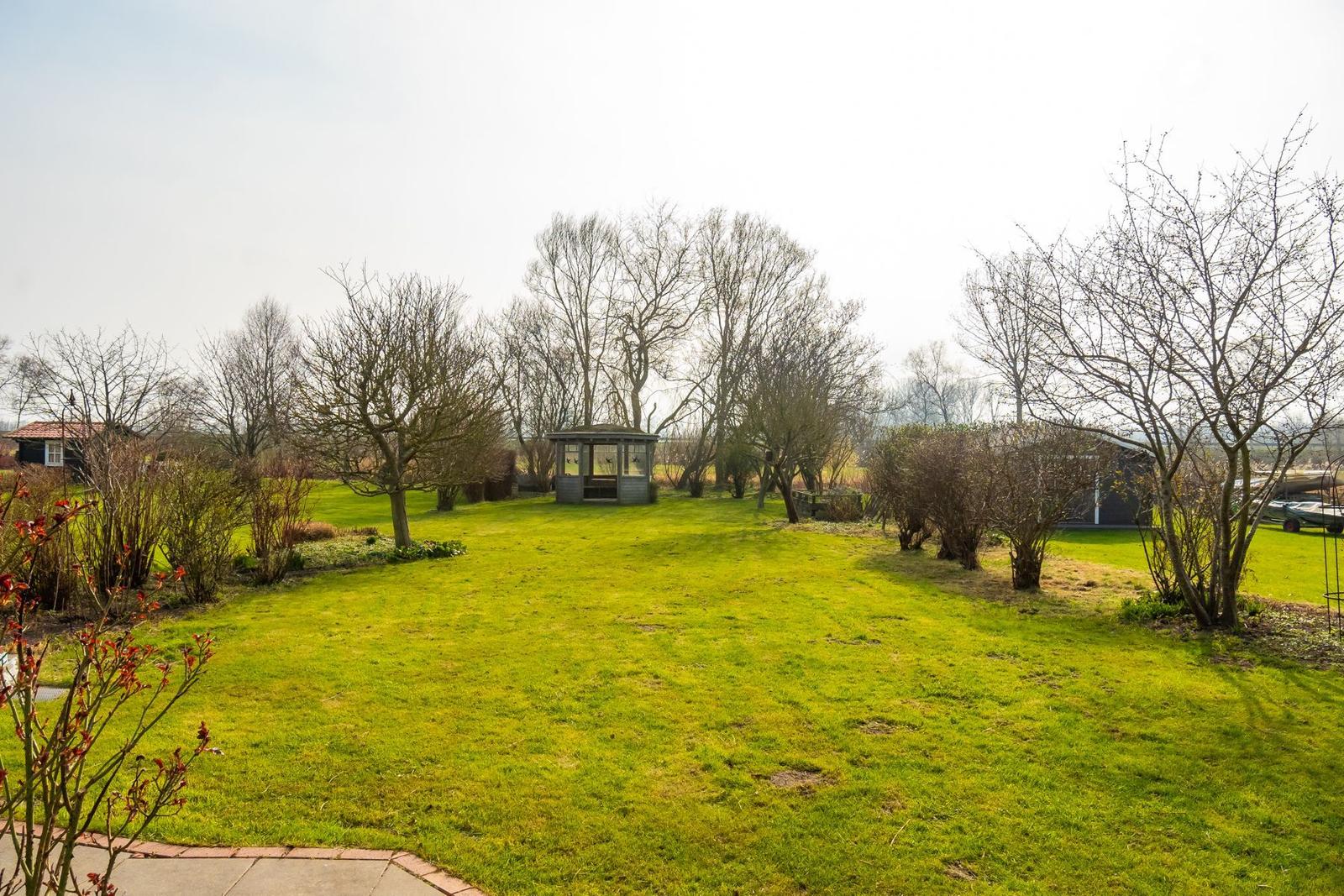 Grüner Garten mit kleinem Pavillon und Bäumen ohne Blätter.