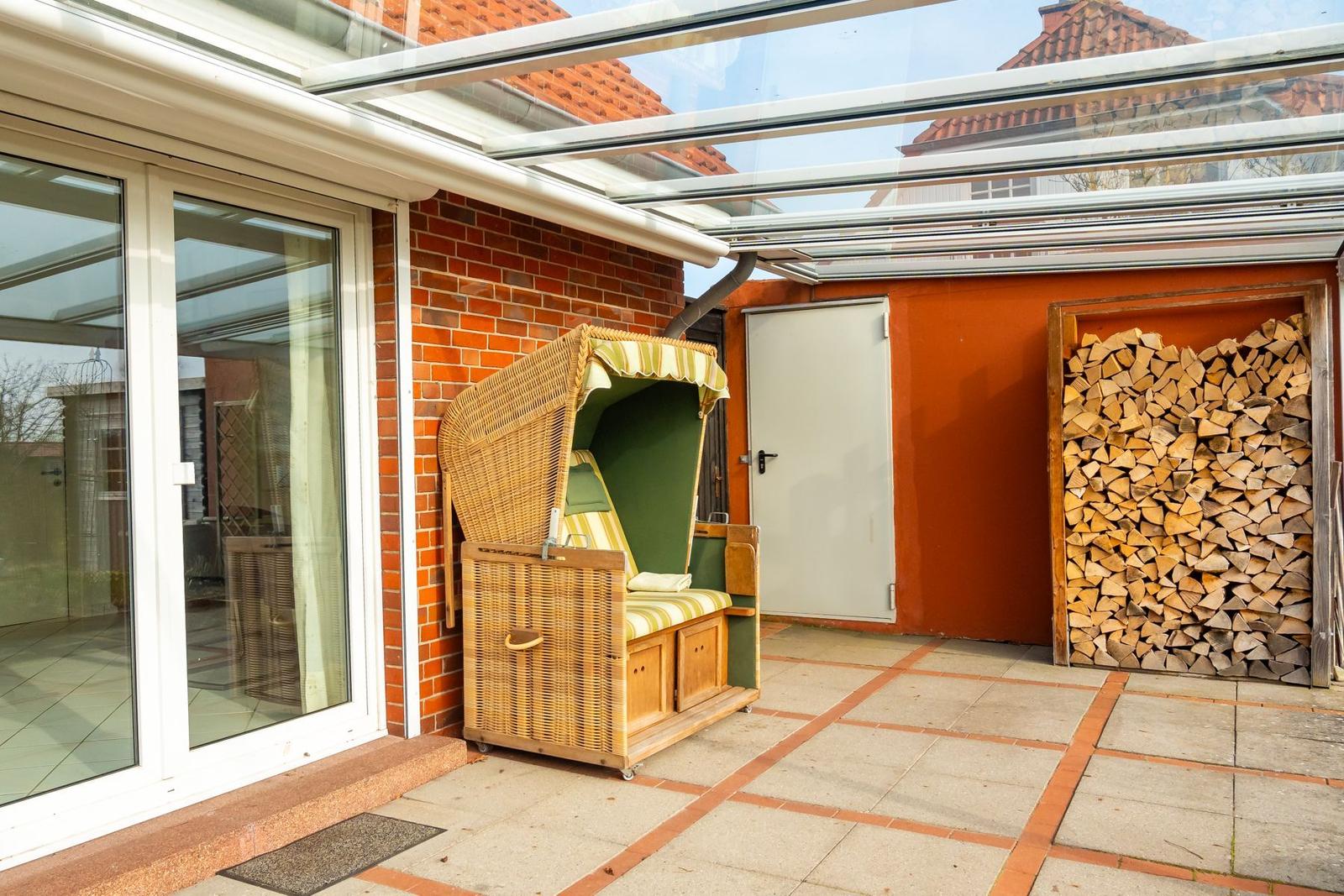 Terrasse mit Rattanliege, Holzstapel und Glasdach. Zugang über Schiebetür.