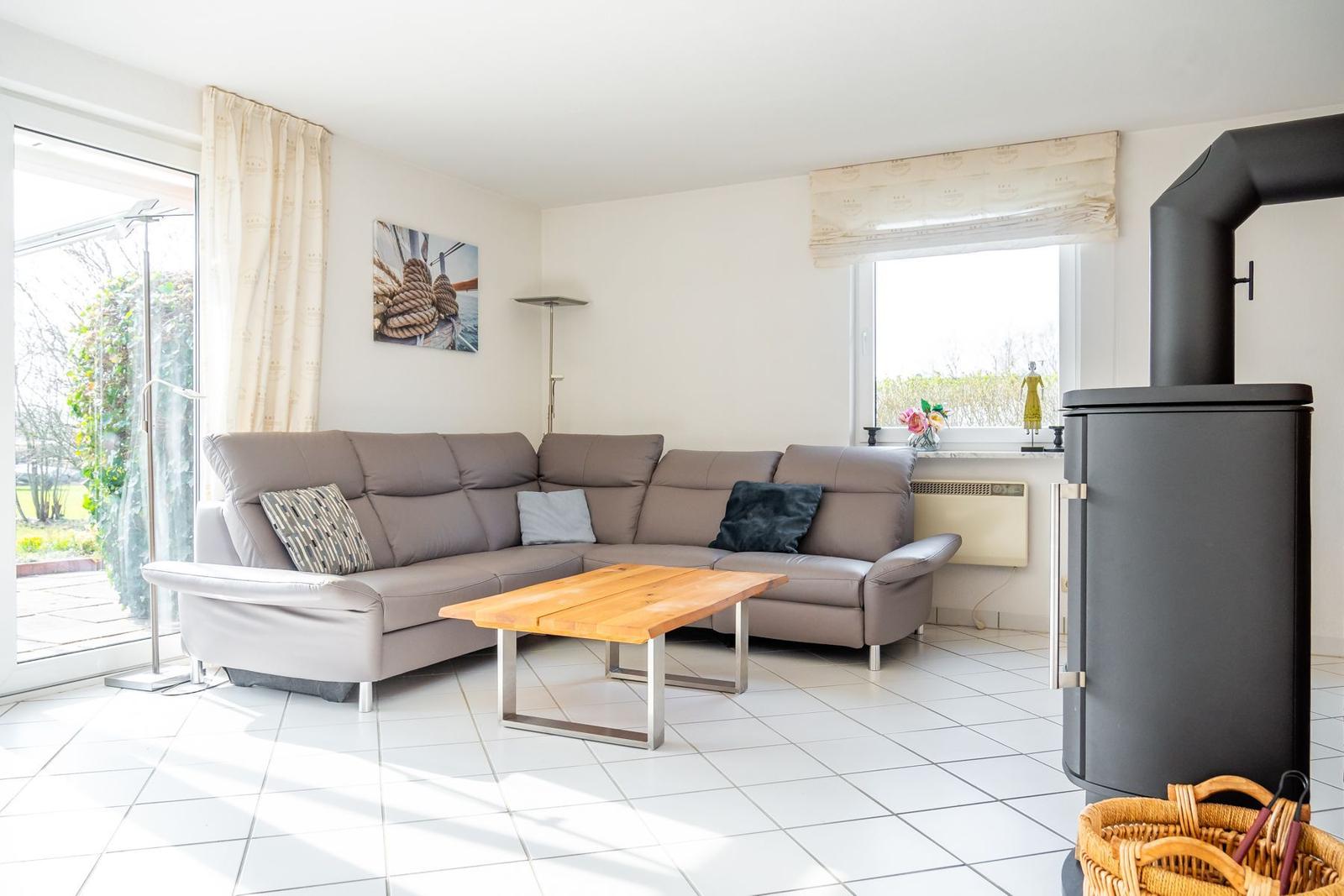 Wohnzimmer mit Ecksofa, Holztisch und Kaminofen. Durchgang zur Terrasse.