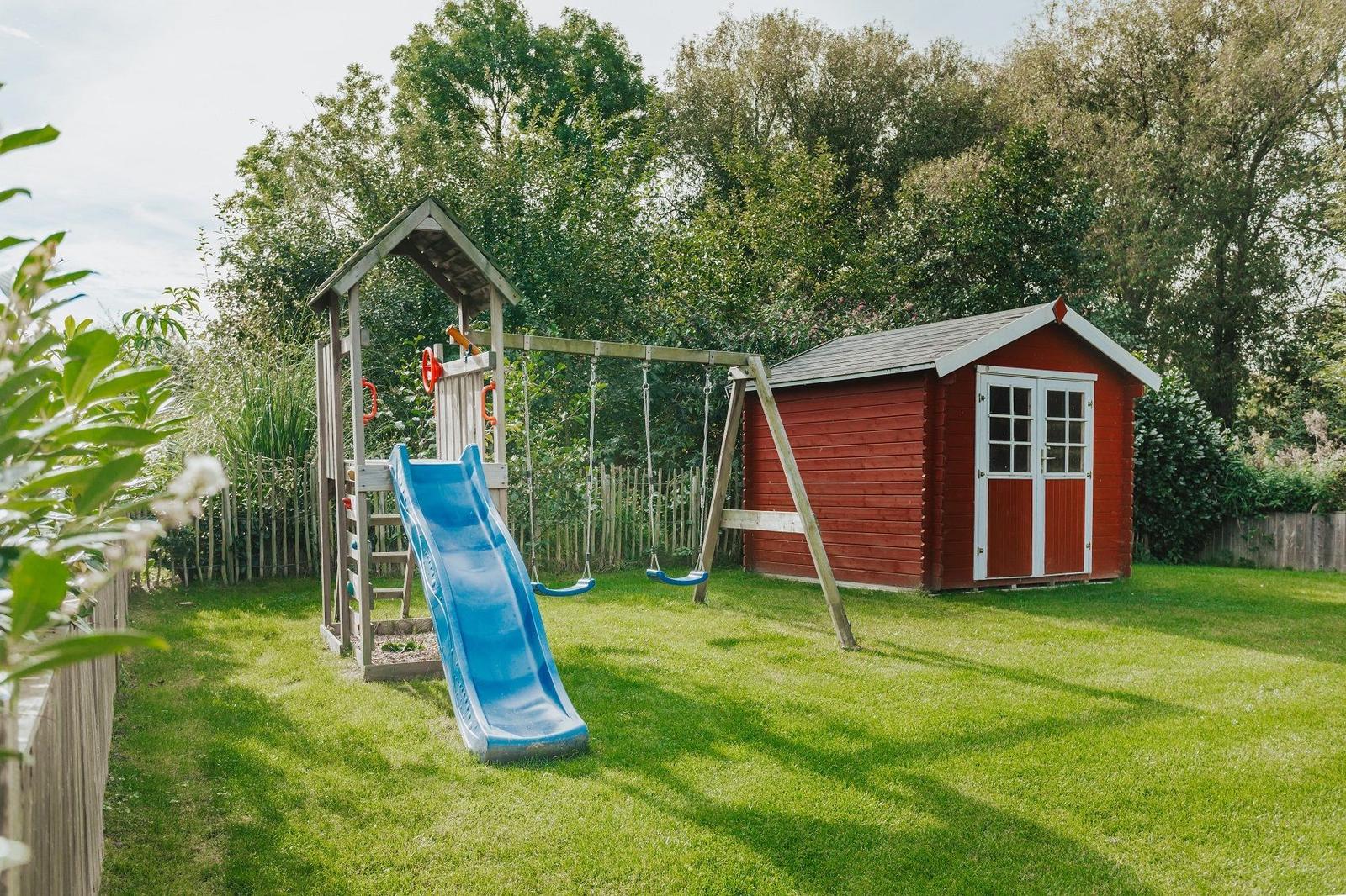 Roter Holzschuppen neben Spielplatz mit Rutsche und Schaukel.