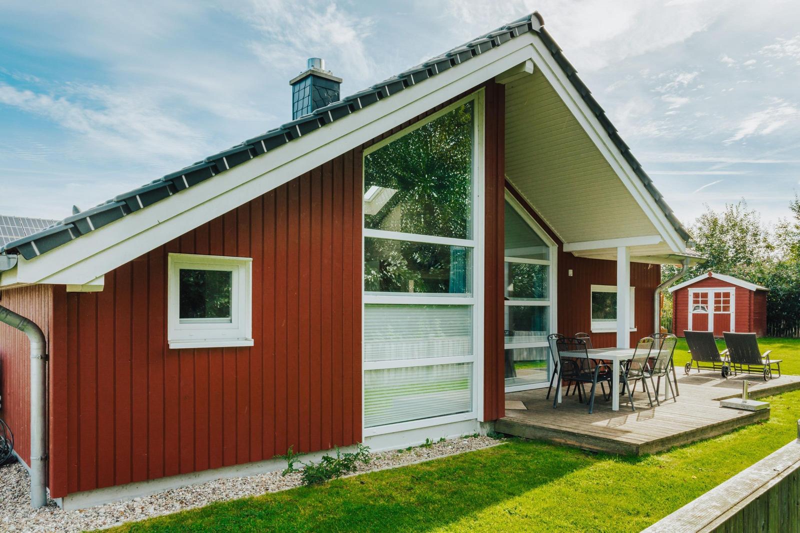 Rotes Holzhaus mit Terrasse und Sitzgelegenheiten im Garten.