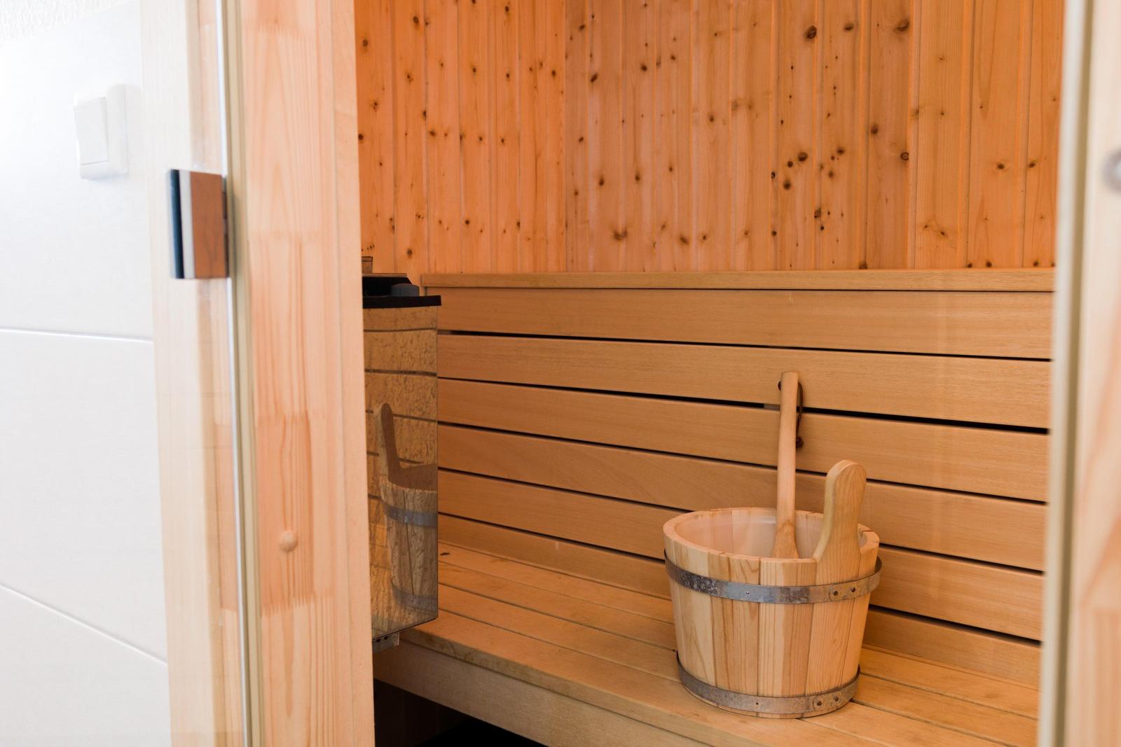 Sauna mit Holzwand, Sitzbank und Eimer mit Löffel.