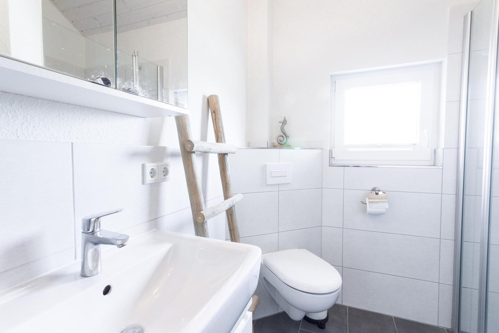 Badezimmer mit Waschbecken, Toilette und Dusche. Holzleiter und Fenster sichtbar.
