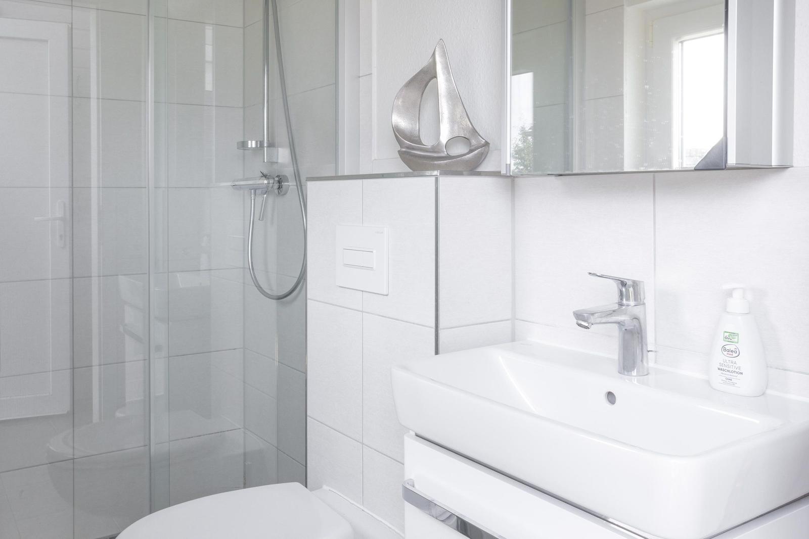 Badezimmer mit Dusche, Waschbecken und Spiegel. Silberne Segeldekoration.