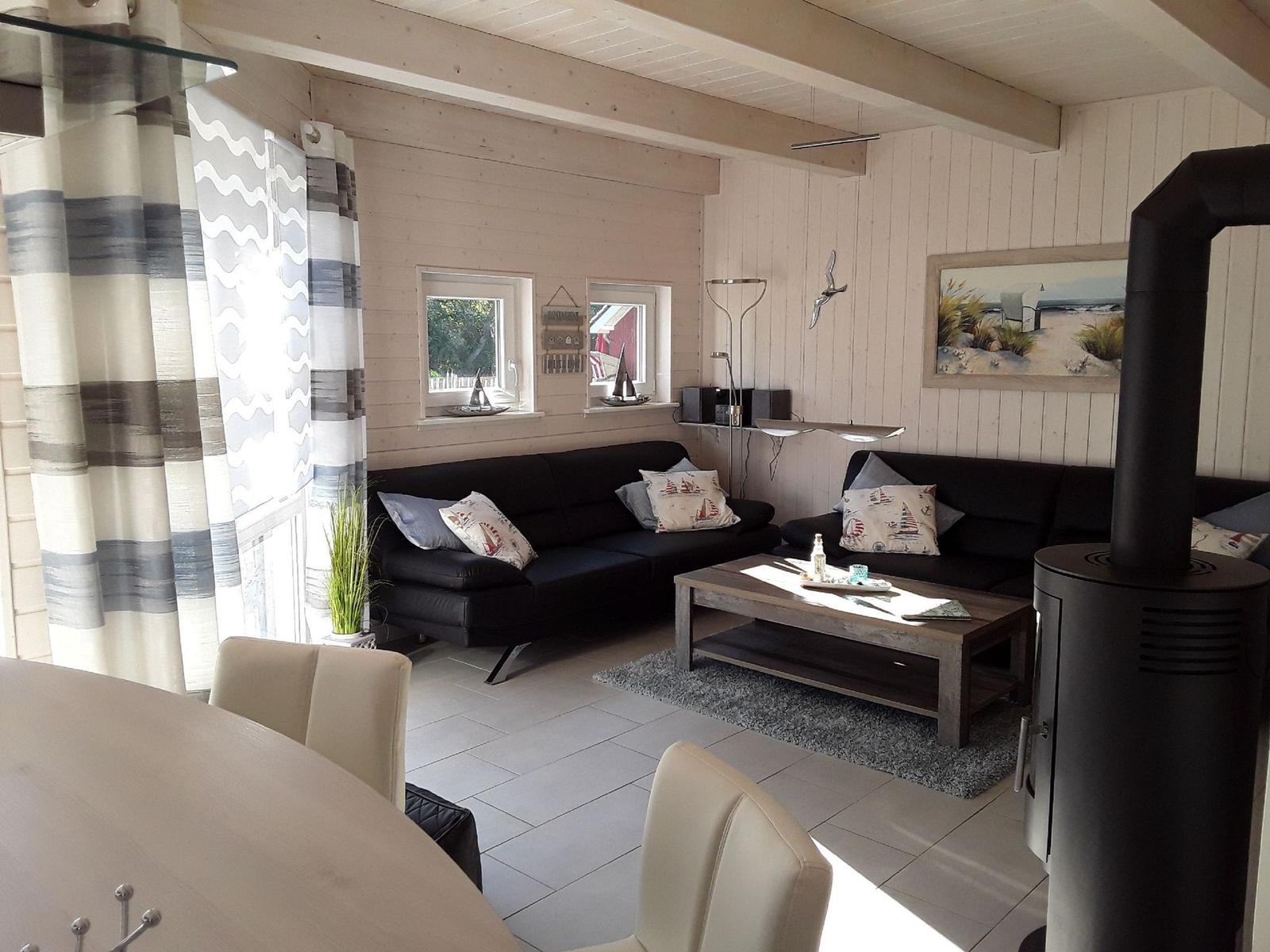 Wohnzimmer mit Sofa, Couchtisch und Kaminofen. Fenster mit Vorhängen und Wandbild.
