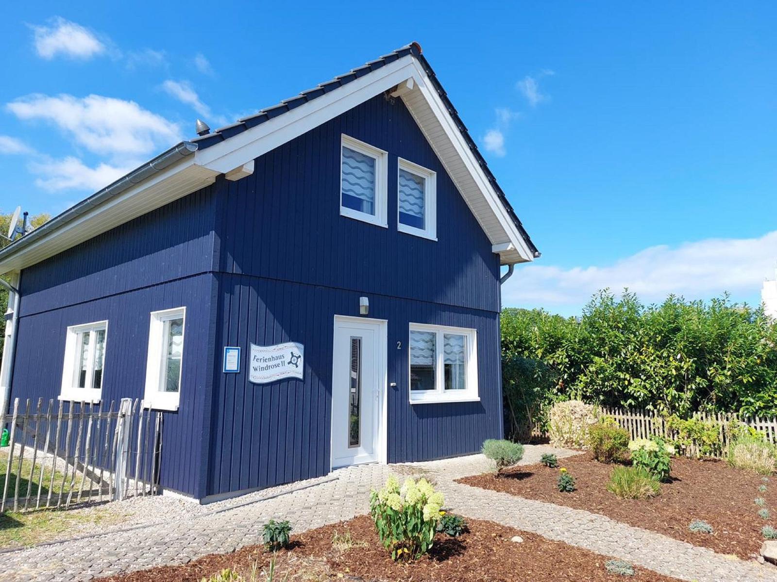 Blau gestrichenes Ferienhaus mit weißen Fenstern und Eingang. Garten mit Beeten und Holzzaun.