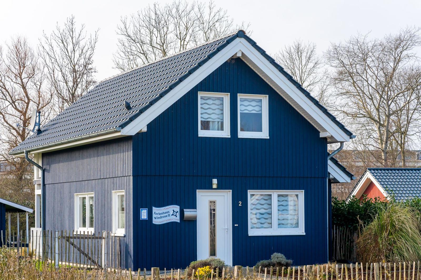 Blau gestrichenes Ferienhaus mit weißen Fensterrahmen und Vordertür. Hintergrund mit kahlen Bäumen.