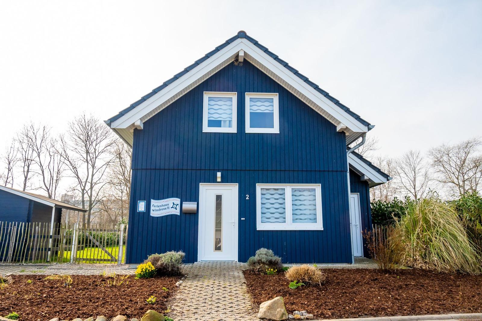 Blau gestrichenes Ferienhaus mit weißer Tür und Fenstern. Gartenweg und Beet mit Pflanzen.
