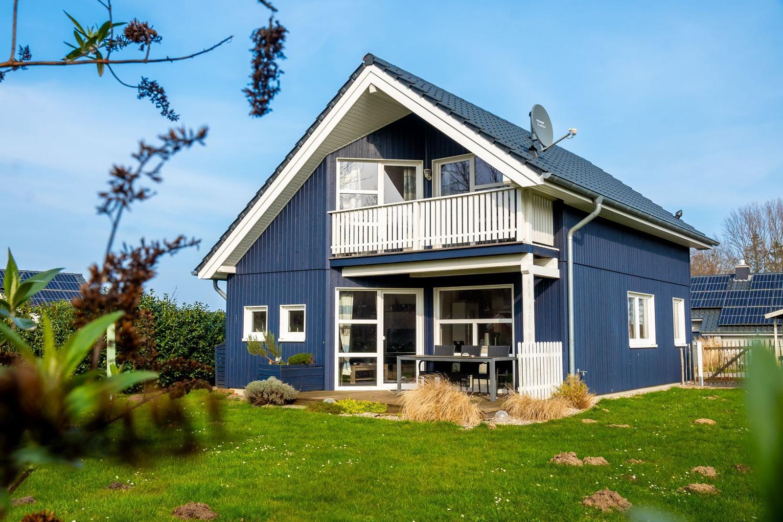 Blau gestrichenes Haus mit Balkon und Garten. Terrasse mit Tisch und Stühlen.