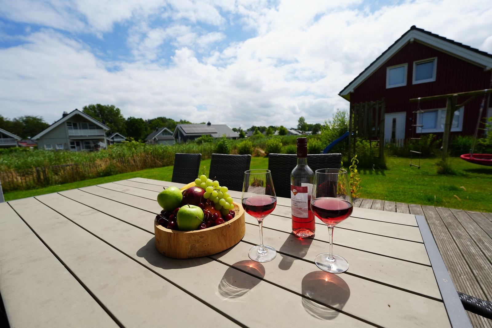 Holztisch mit Wein, Obst und Blick auf Haus und Garten.