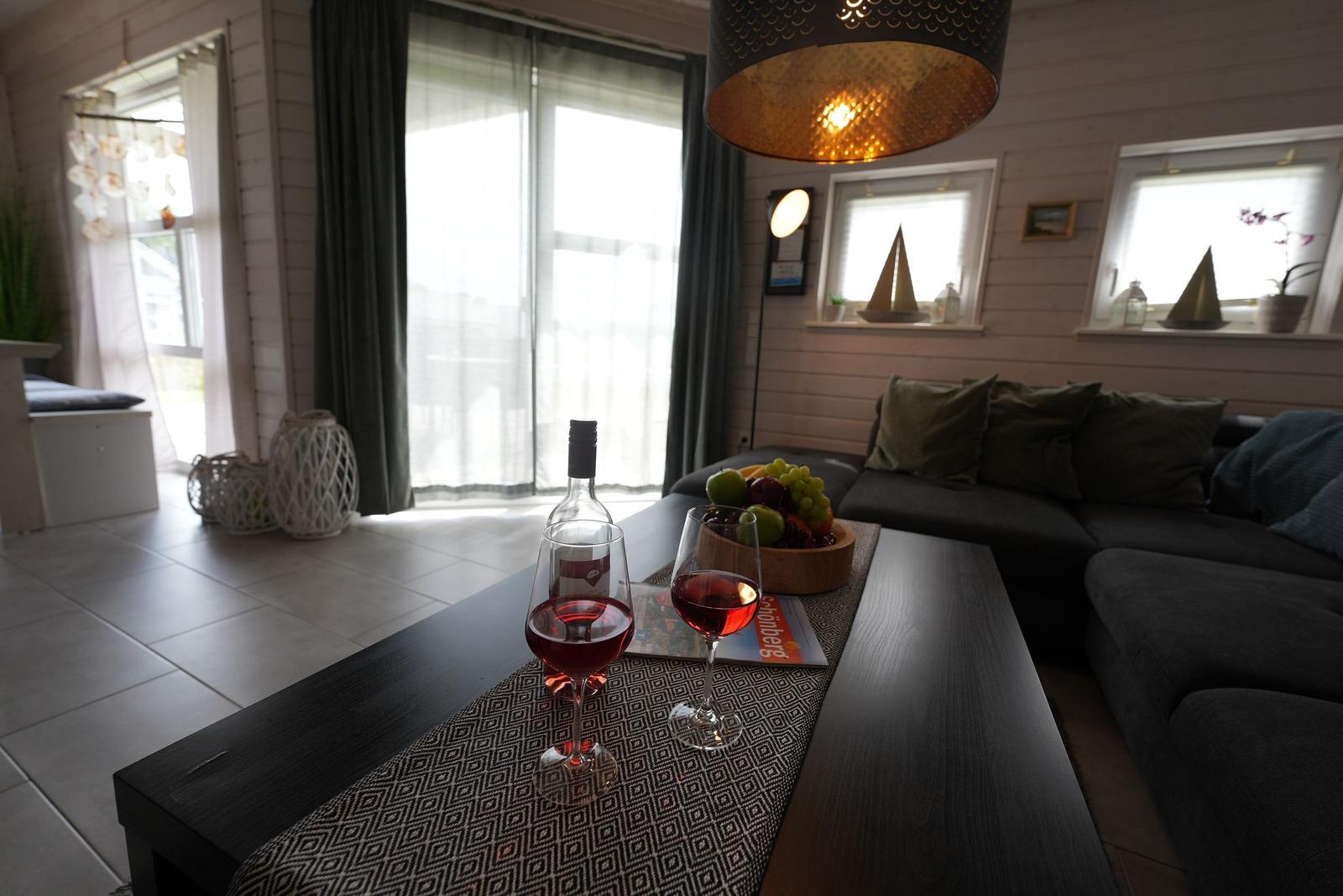 Wohnzimmer mit Sofa, Tisch und Wein. Fenster und Deckenleuchte sichtbar.