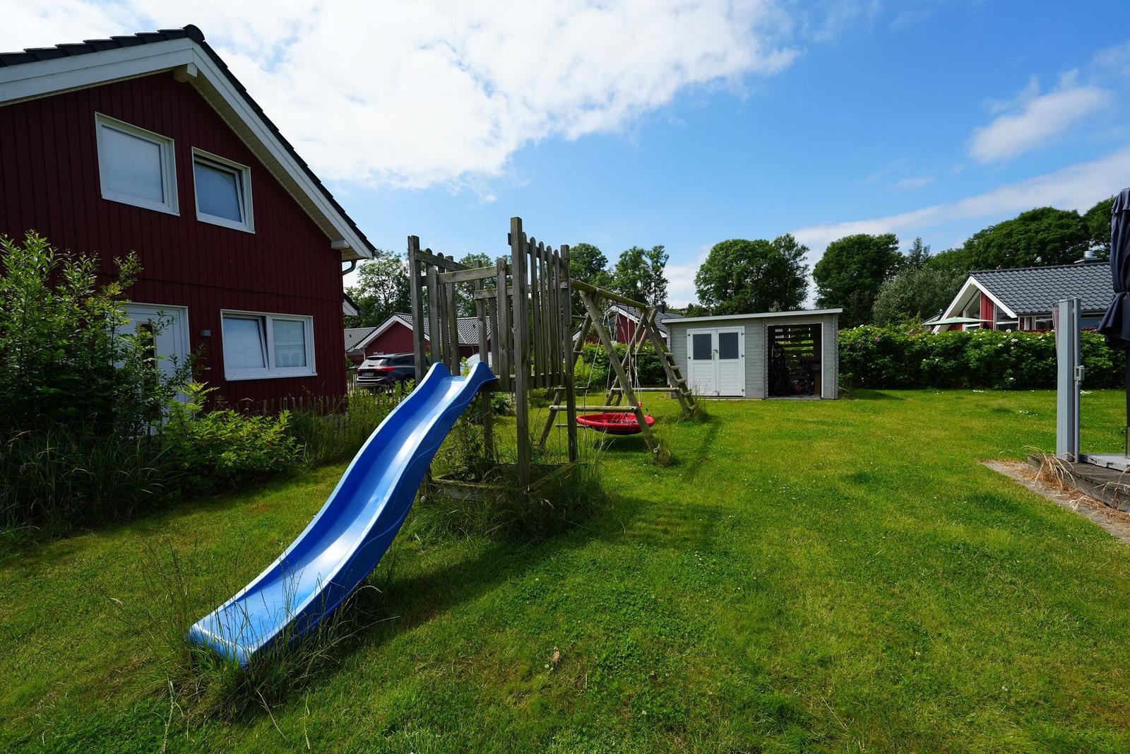 Roter Ferienhaus mit Spielplatz und blauer Rutsche im Garten.