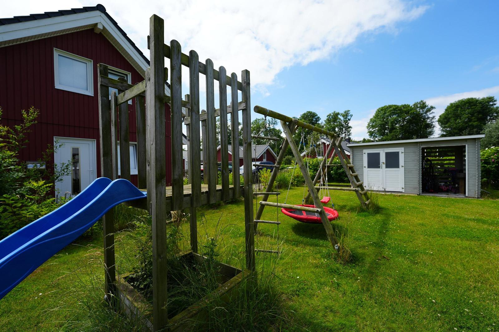 Hinterhof mit Spielplatz, Rutsche und Schaukel. Rotes Haus und graue Garage sind sichtbar.