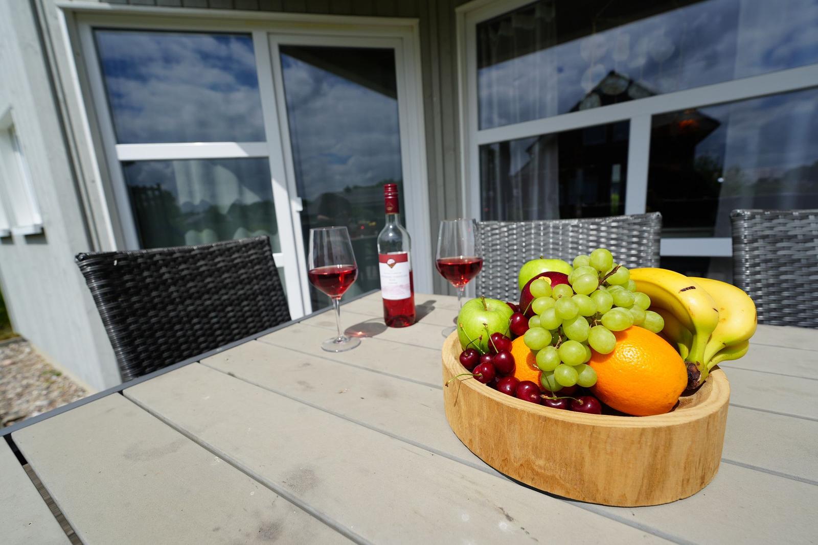 Holztablett mit Obst und Wein auf Terrasse vor Haus.