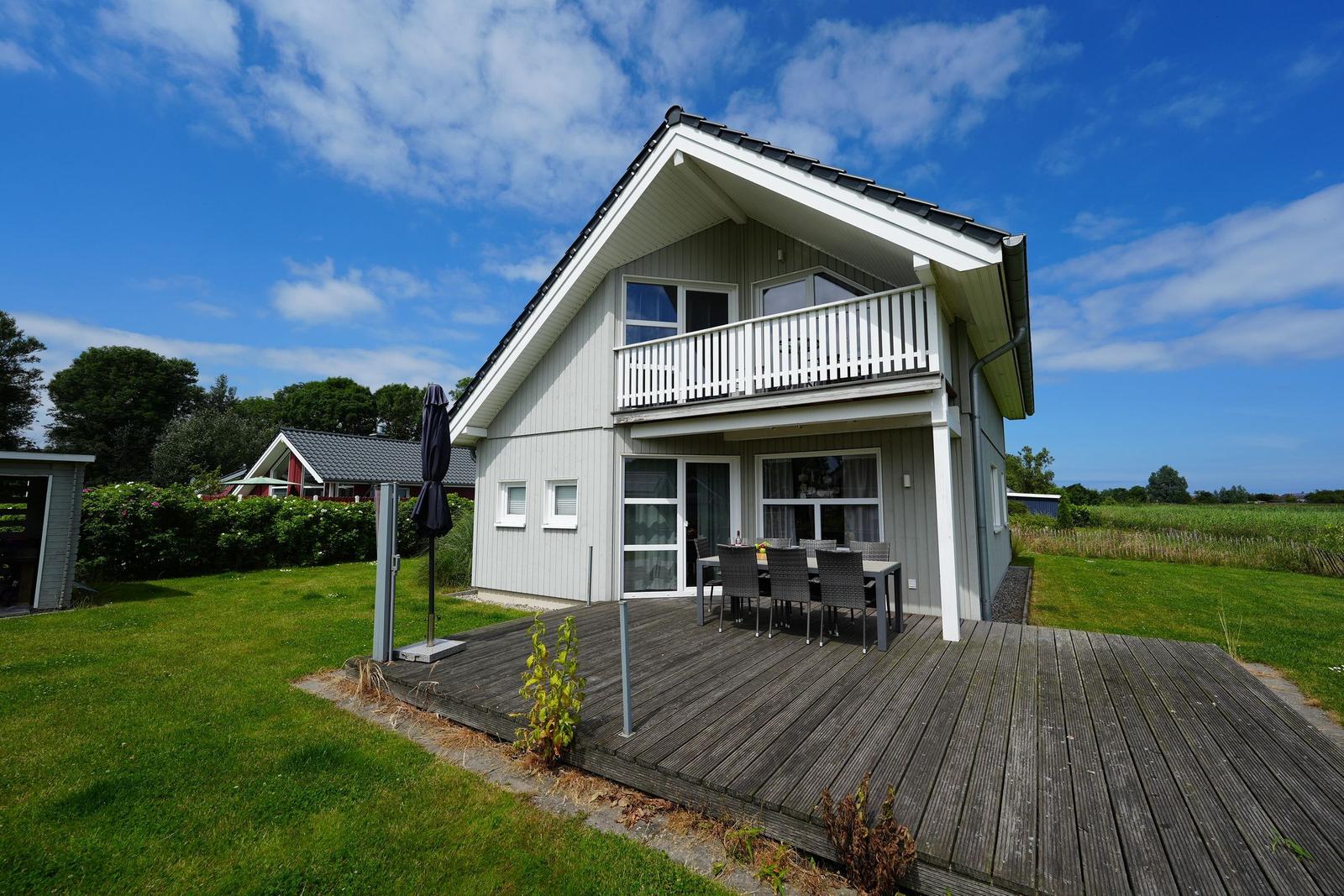 Ein zweistöckiges Haus mit Balkon und Terrasse mit Sitzgelegenheiten.