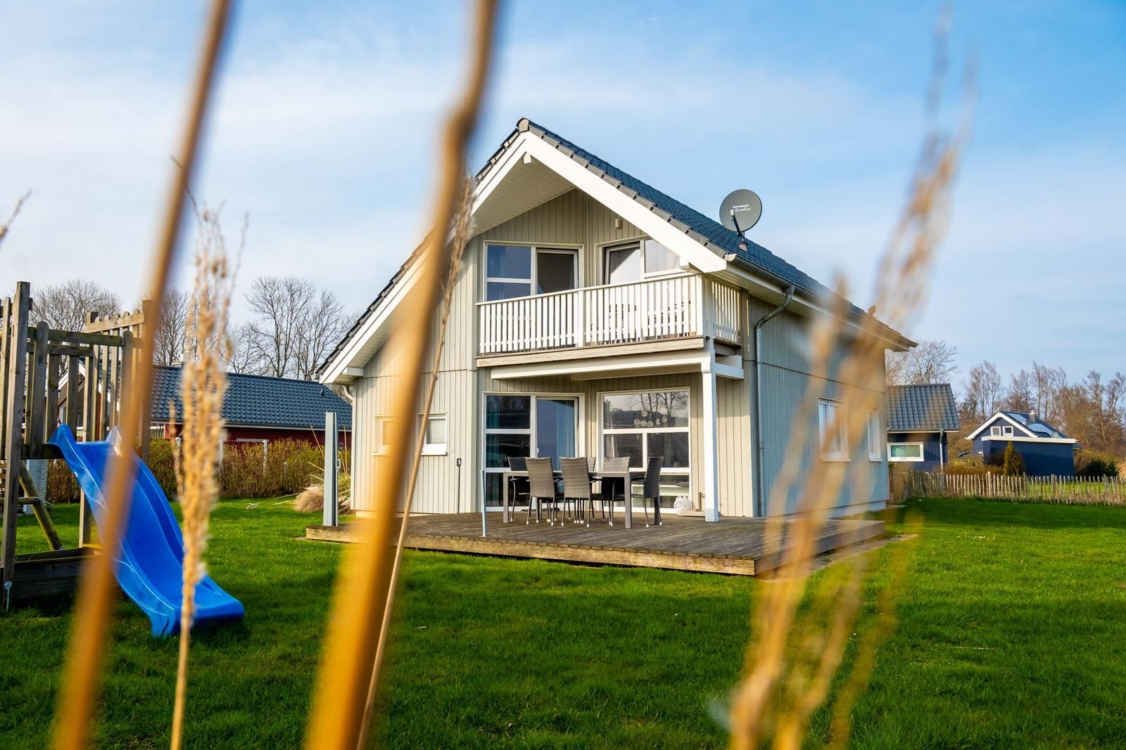 Ein zweistöckiges Haus mit Balkon, Terrasse und Garten mit Spielplatz.