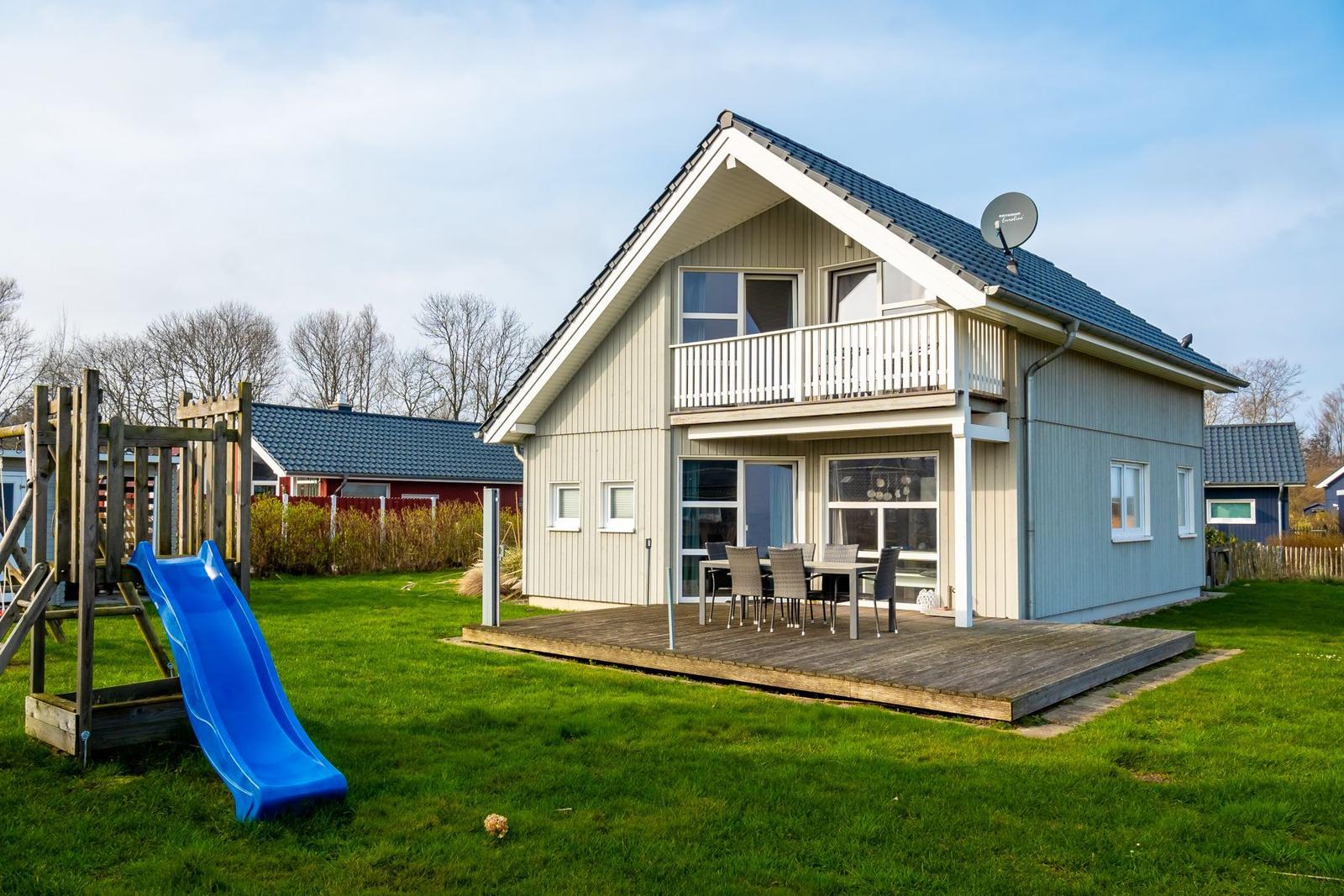 Haus mit Balkon, Terrasse und Spielplatz mit Rutsche.