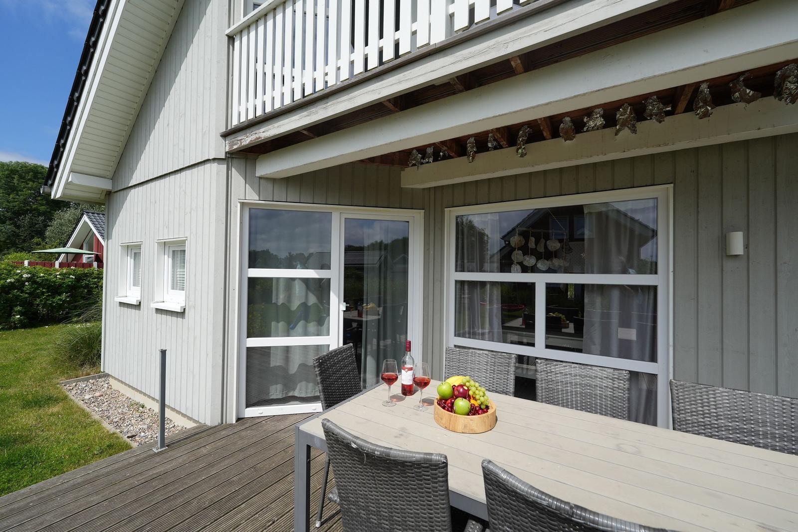 Terrasse mit Tisch, Stühlen und Obst. Hintergrund: Haus mit Fenstern und Balkon.