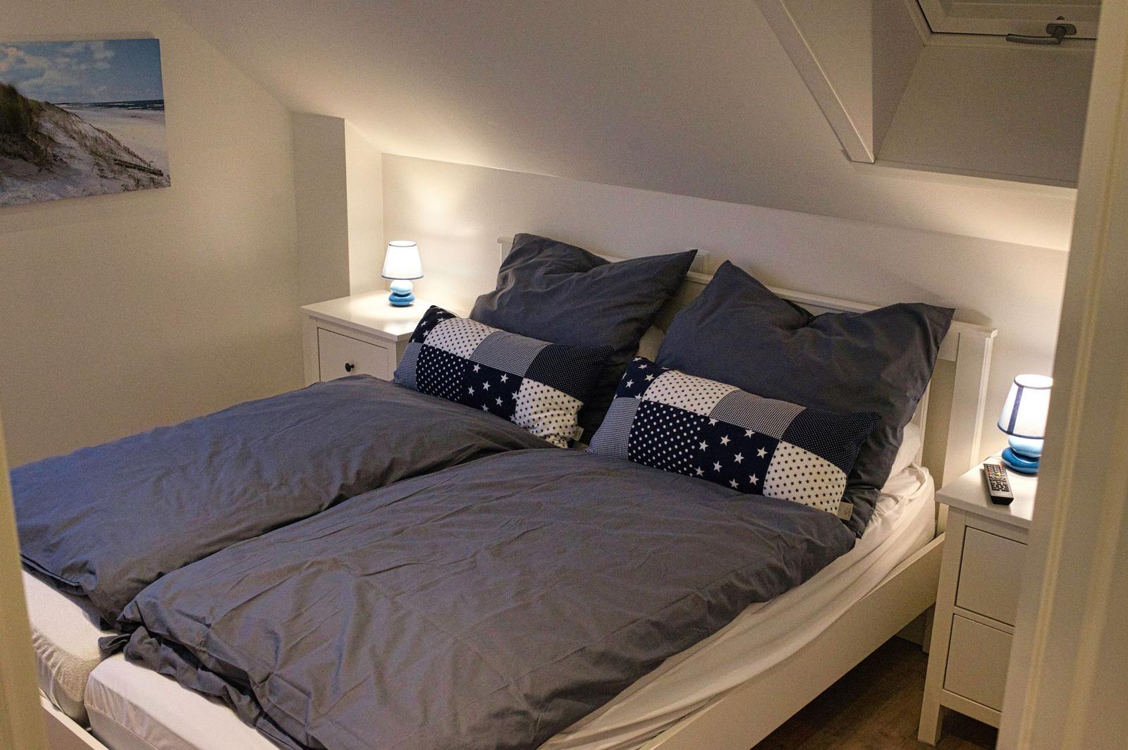 Doppelbett mit Kissen und Nachttischen unter Dachschrägen