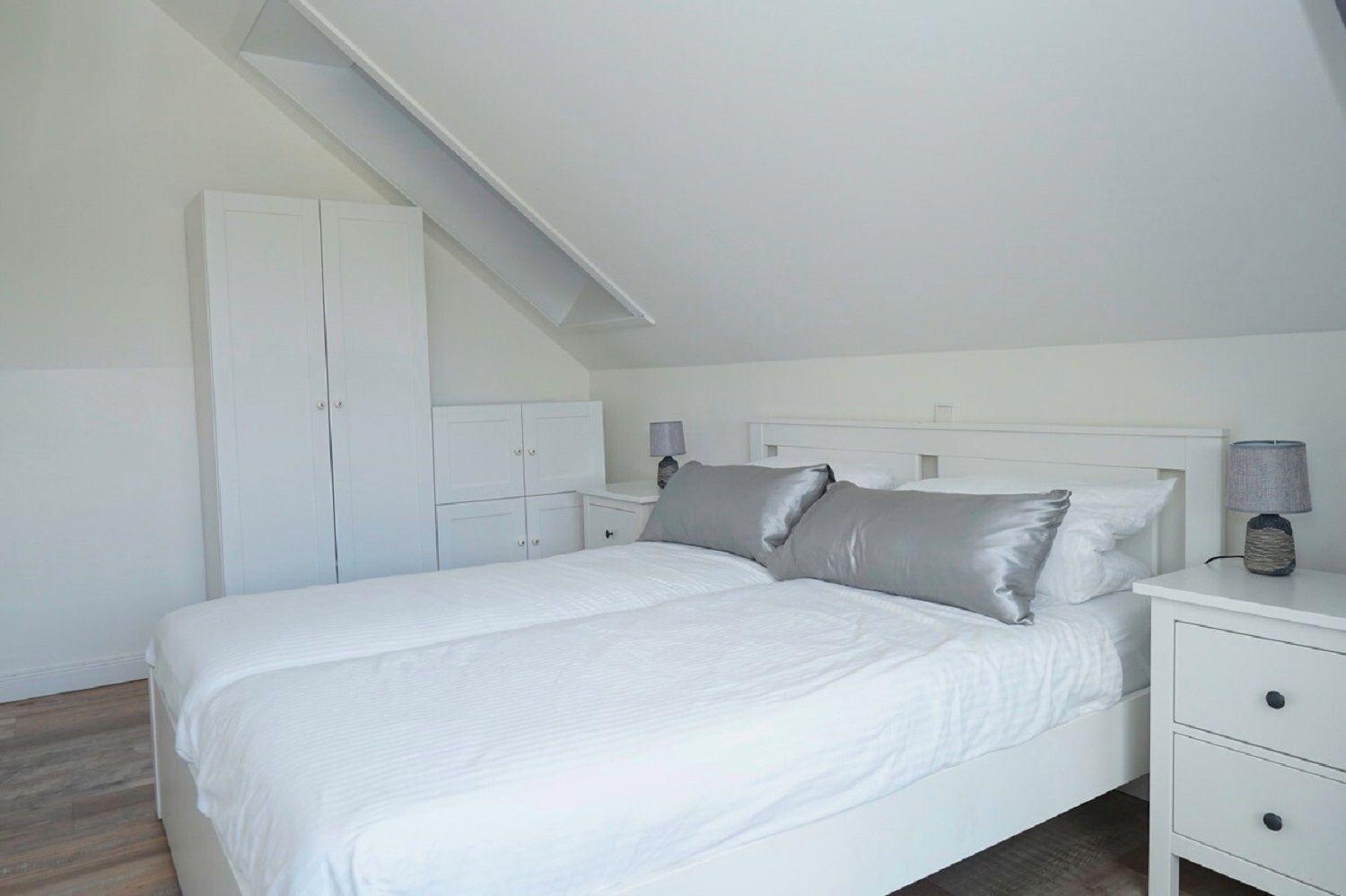 Schlafzimmer mit Dachschrägen, weißem Bett und Nachttischen.