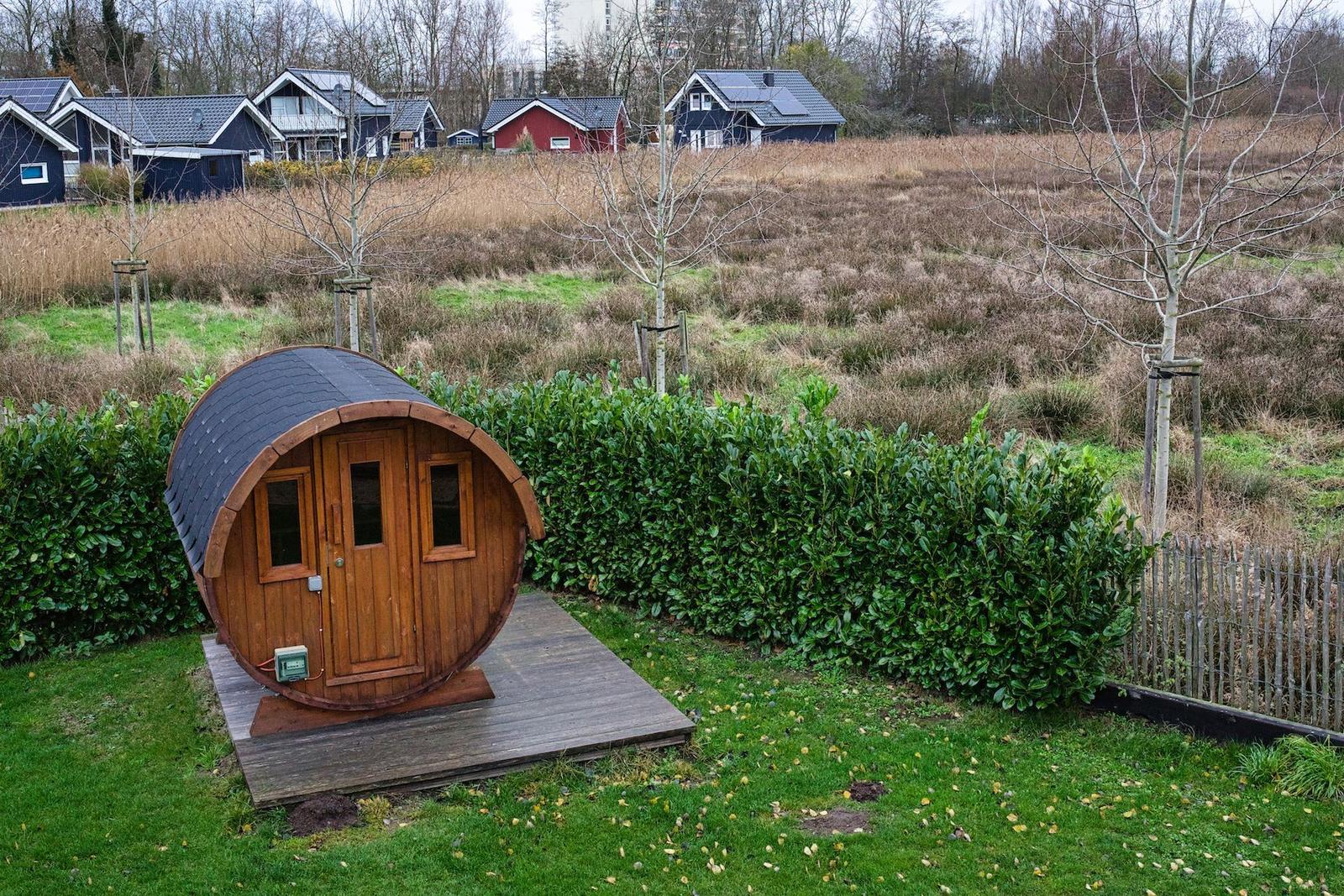 Holzbarrel-Hütte auf Holzplattform mit grünem Rasen und Hecke im Hintergrund.