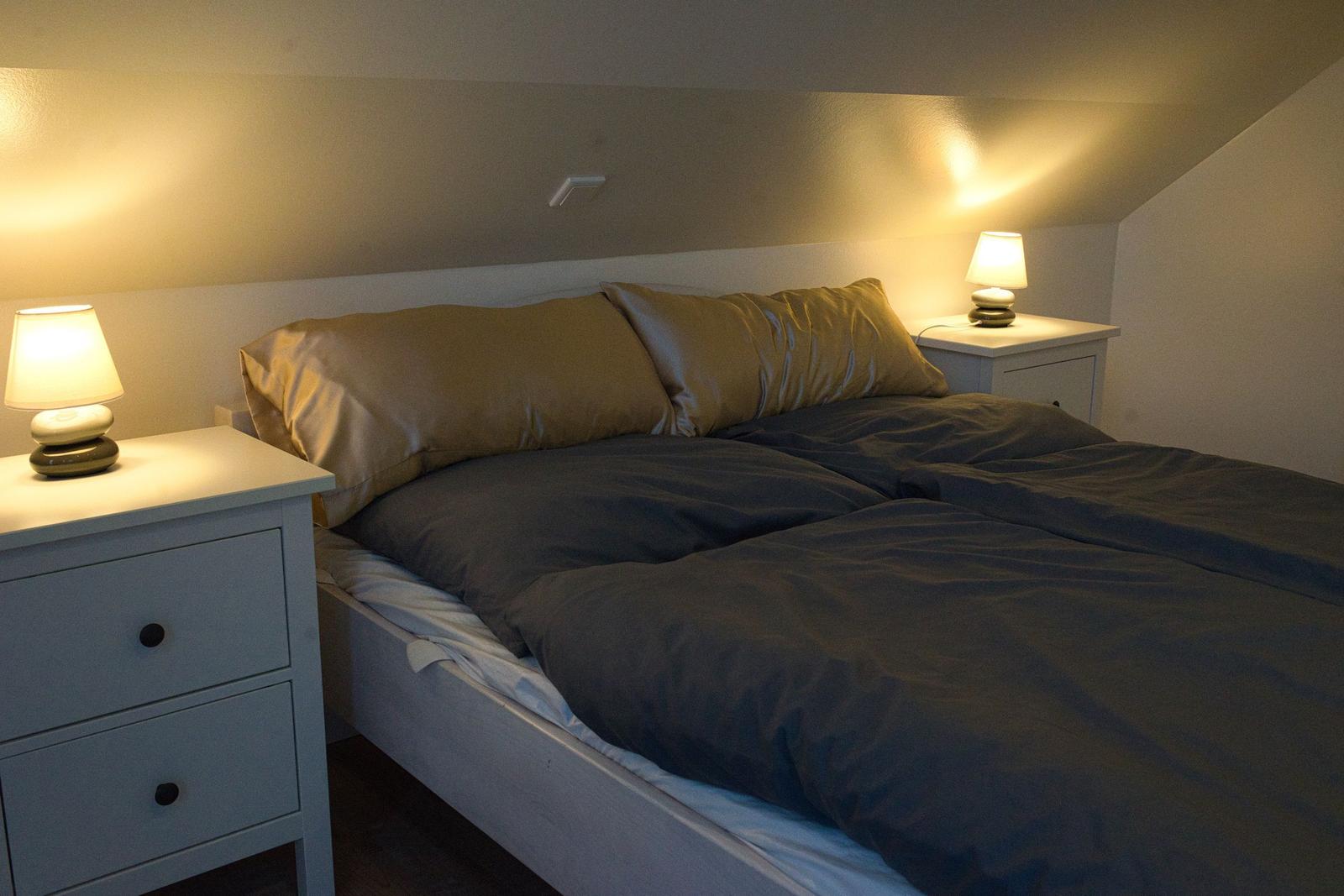 Doppelbett mit zwei Nachttischen und Lampen unter schrägem Dach