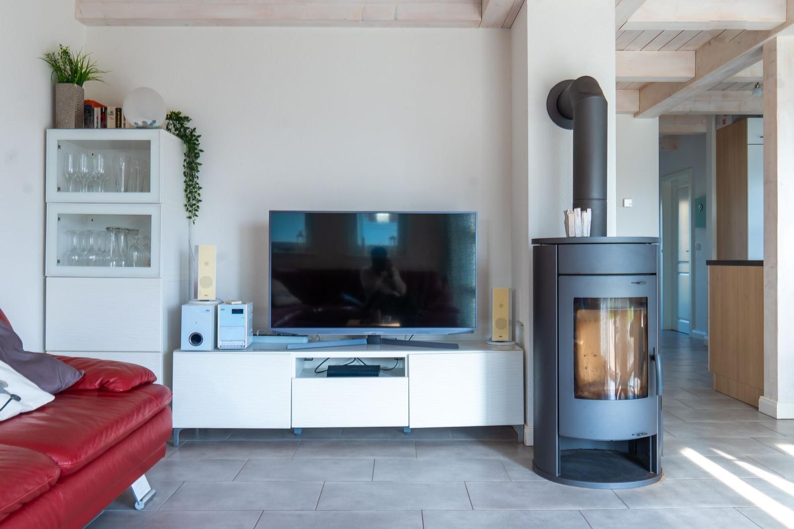 Wohnzimmer mit rotem Sofa, TV und Kaminofen.