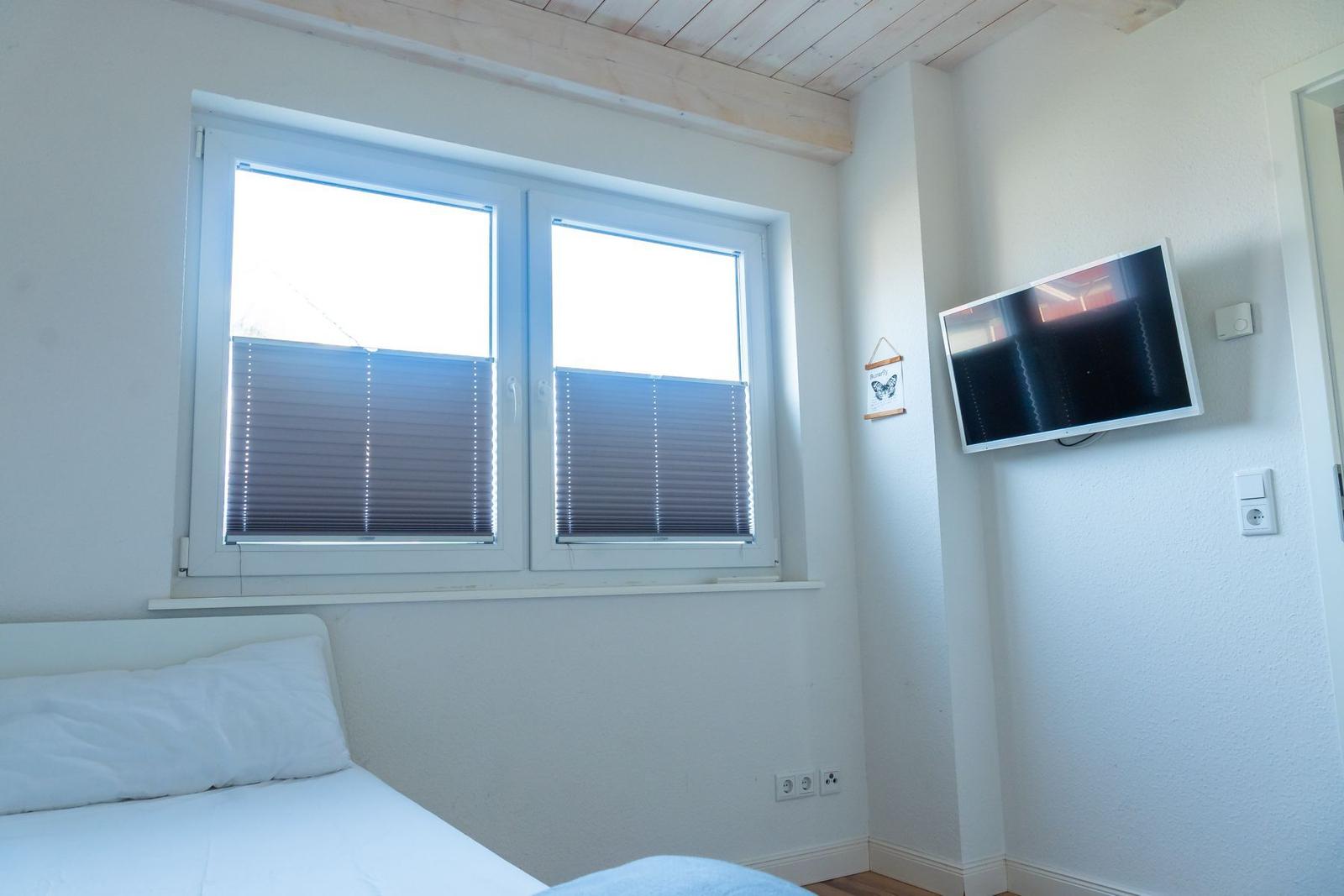 Zimmer mit Bett, Fenster und Wandfernseher.