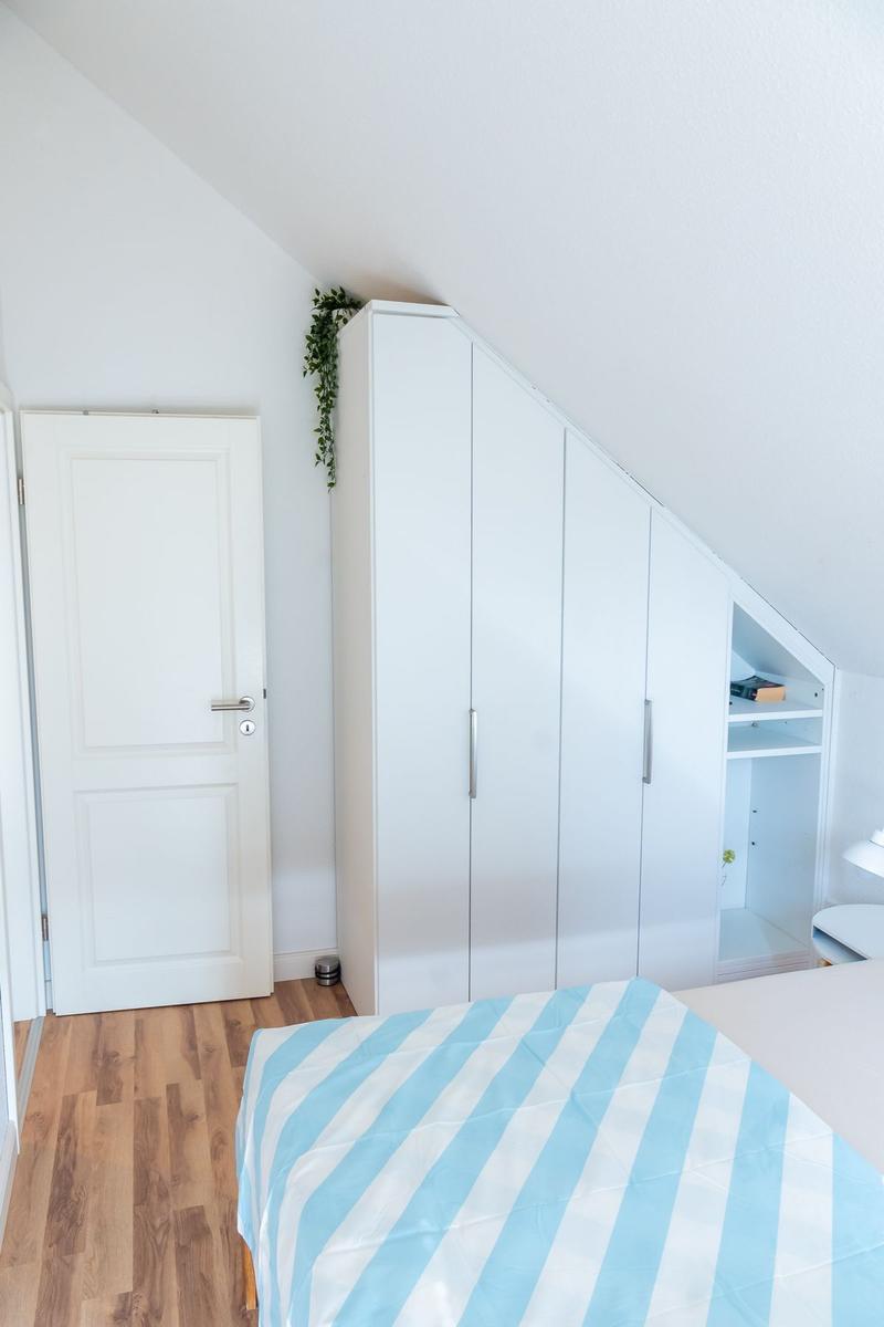 Schlafzimmer mit Dachschrägen, weißer Schrank und Bett mit Streifenbezug.