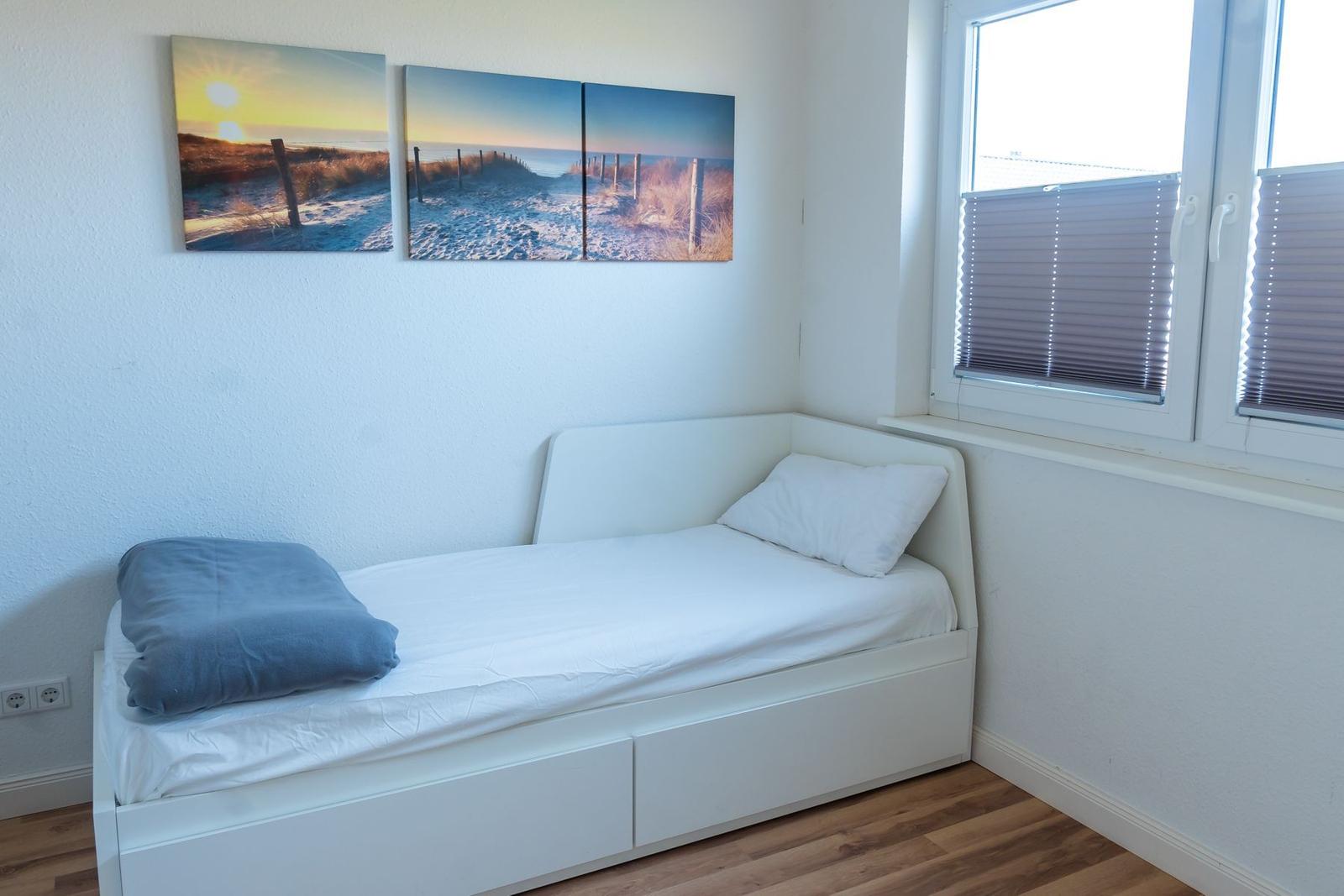 Schlafzimmer mit weißem Bett, Fenster und Wandbildern.